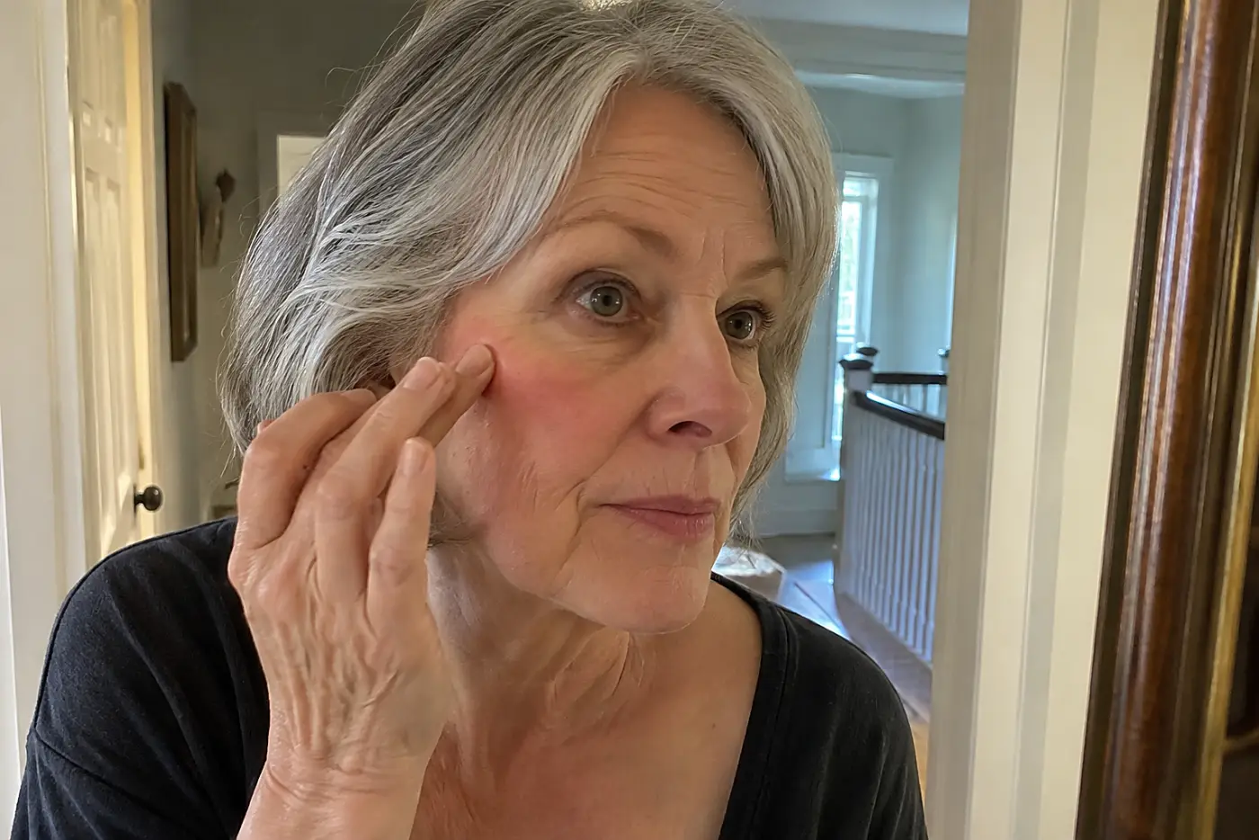 Woman blending liquid blush while looking into a hallway mirror.
