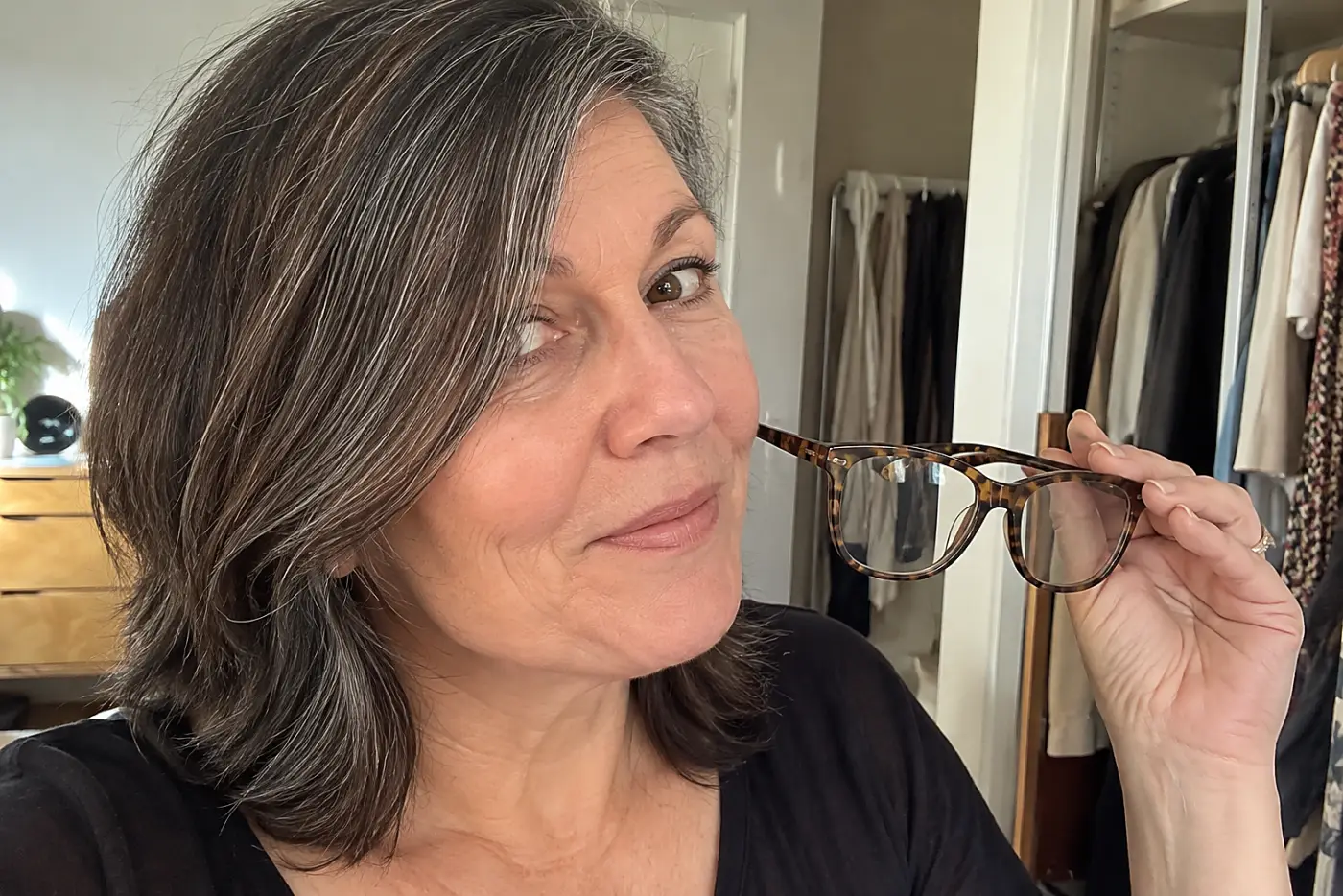 Woman holding tortoiseshell glasses beside her face in a dressing room.