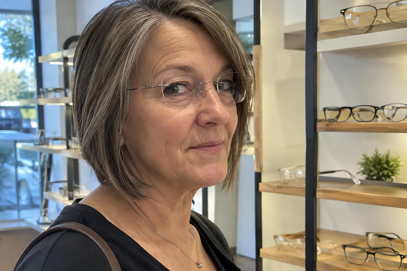 Woman walking past shelves in an optical shop while wearing rimless glasses.