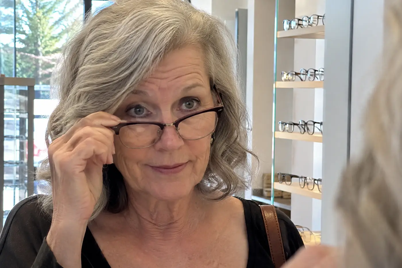 Woman comparing browline frames with her reflection in an optical shop mirror.