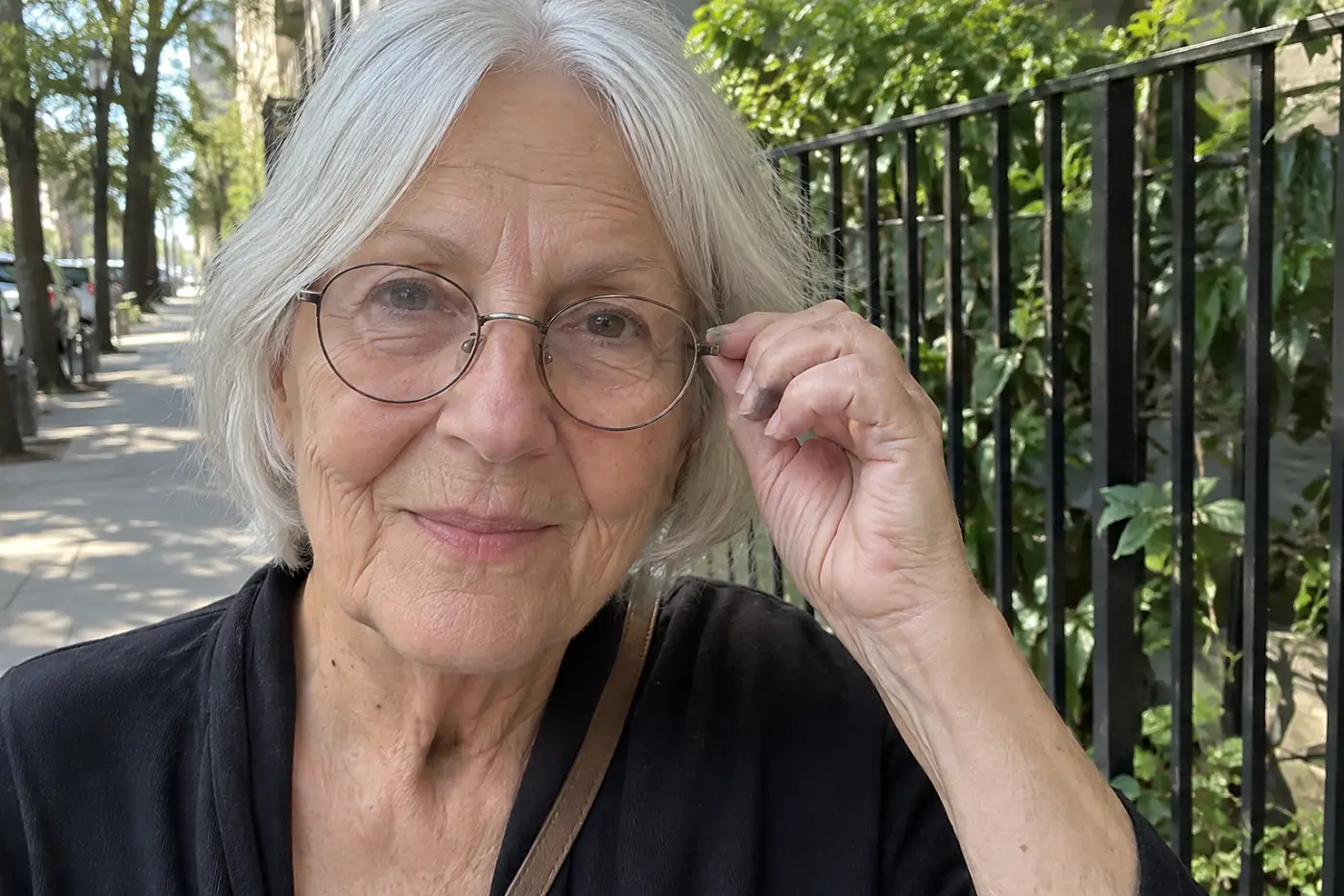 Woman adjusting round metal glasses outside a neighborhood bookstore.
