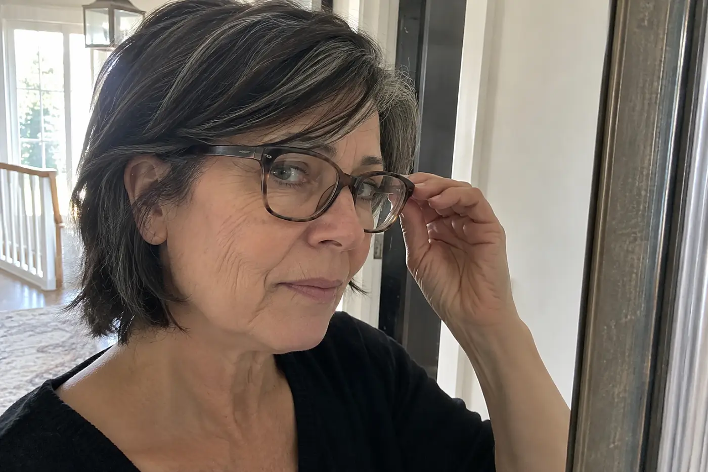 Woman checking the side of thin acetate glasses in a hallway mirror.