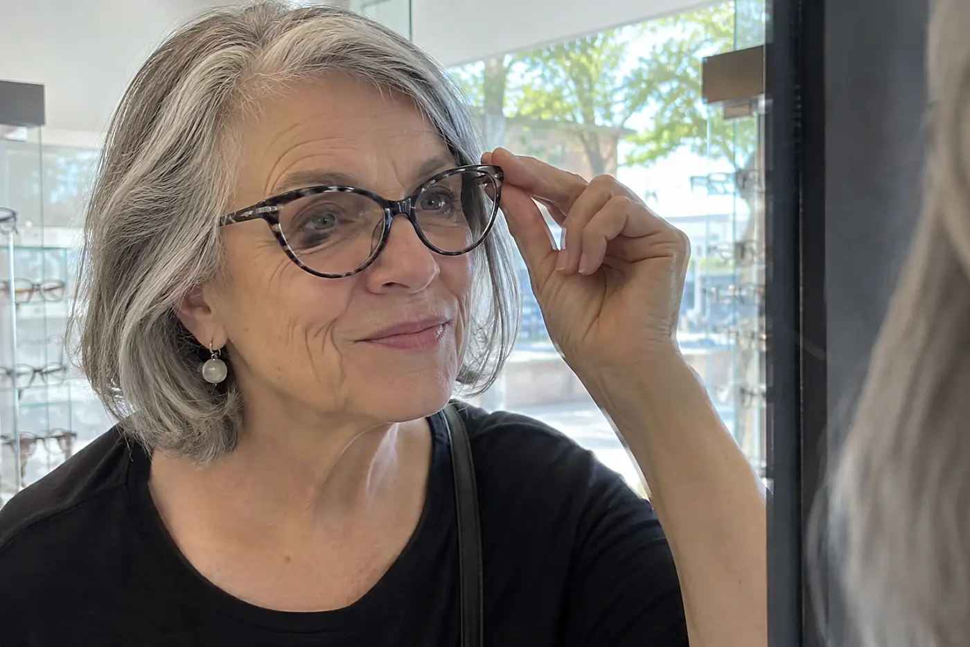 Woman trying on cat-eye glasses in front of a mirror at an optical shop.