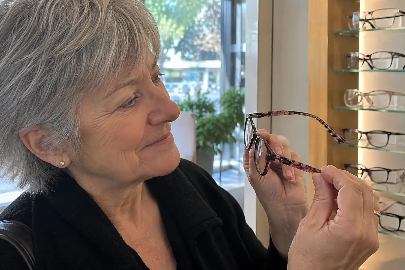Woman inspecting the temples of patterned acetate frames at an optical shop.
