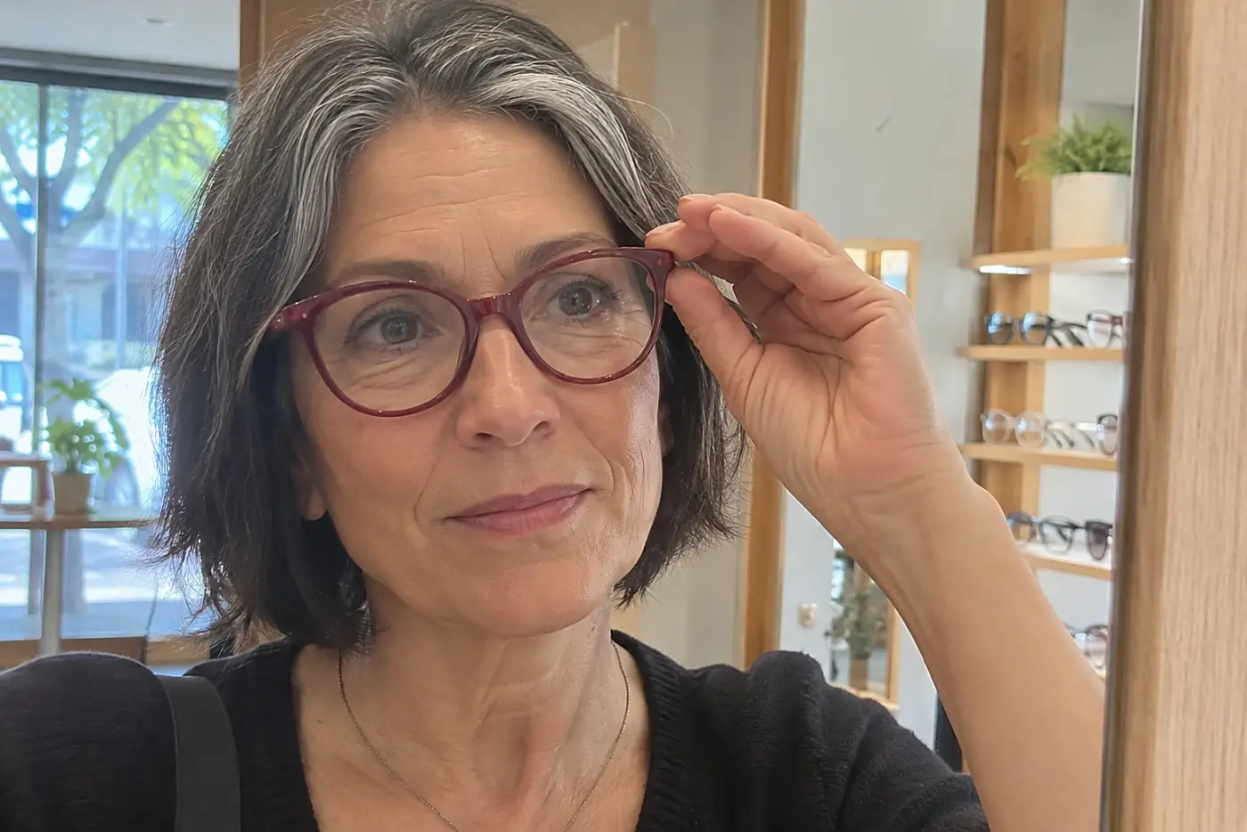 Woman trying on deep red glasses in front of an optical shop mirror.