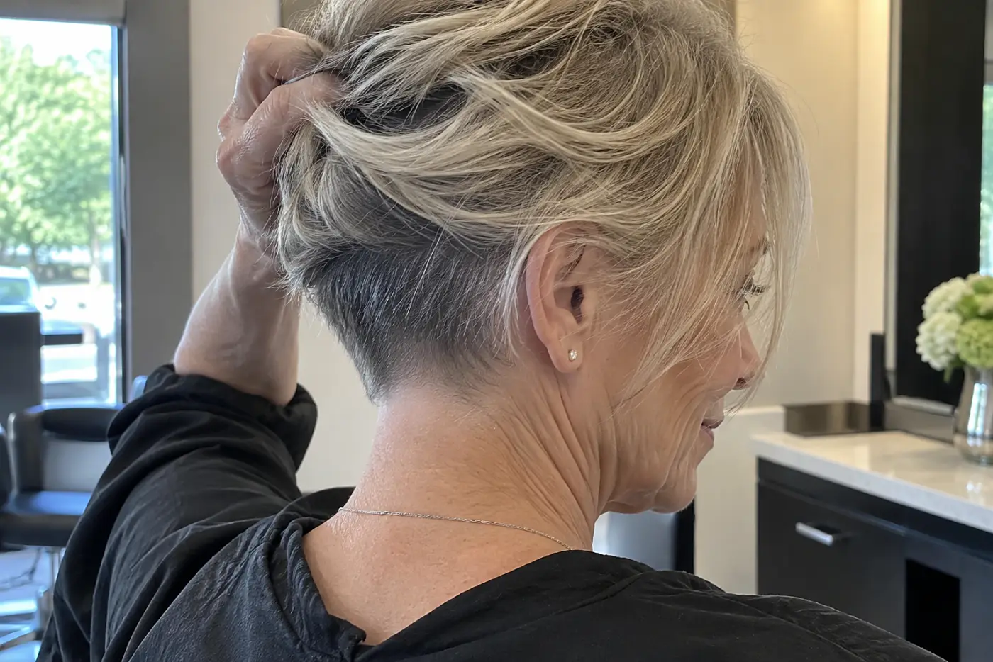 A woman lifts the back of her short bob to show her nape at a salon.