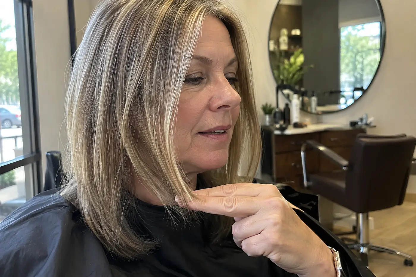 A woman marks her preferred cutting line with her fingers at a salon station.