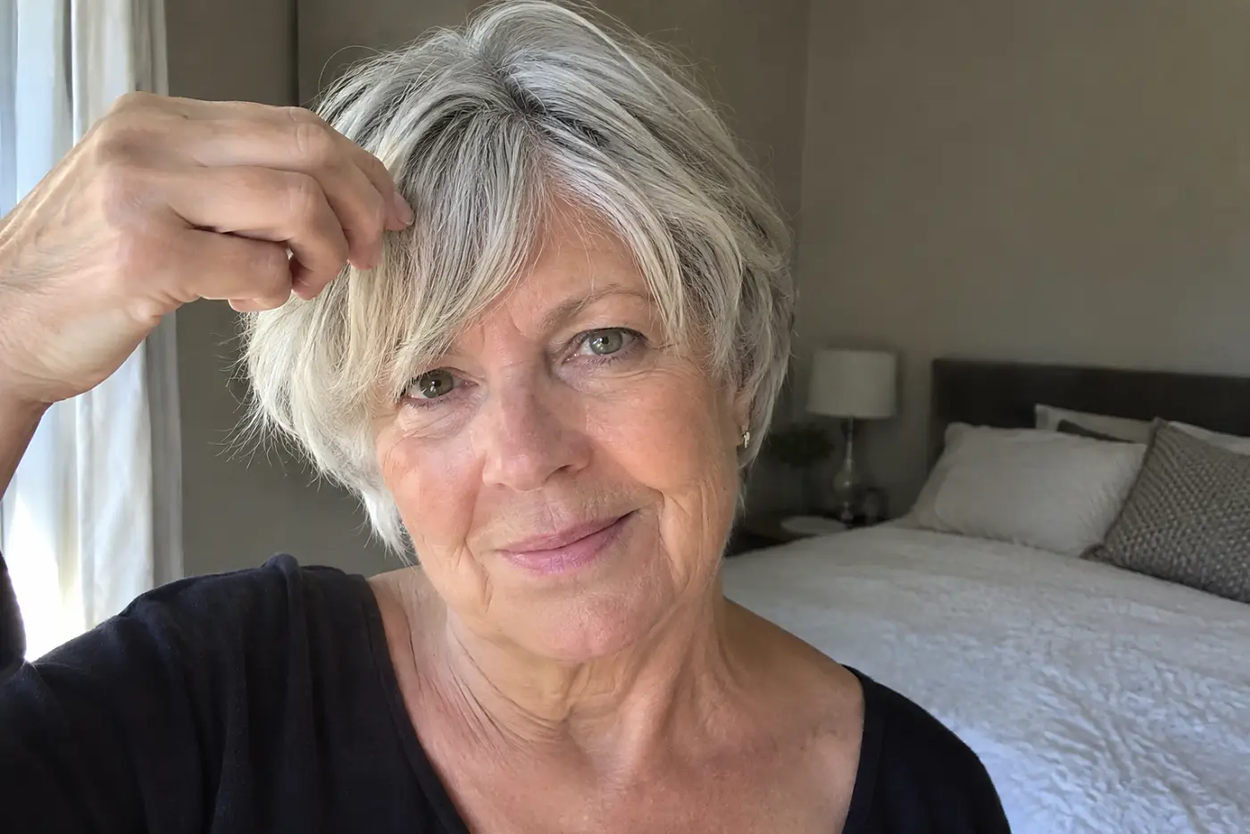 A woman holds a shallow front section of hair across her forehead in a bedroom.