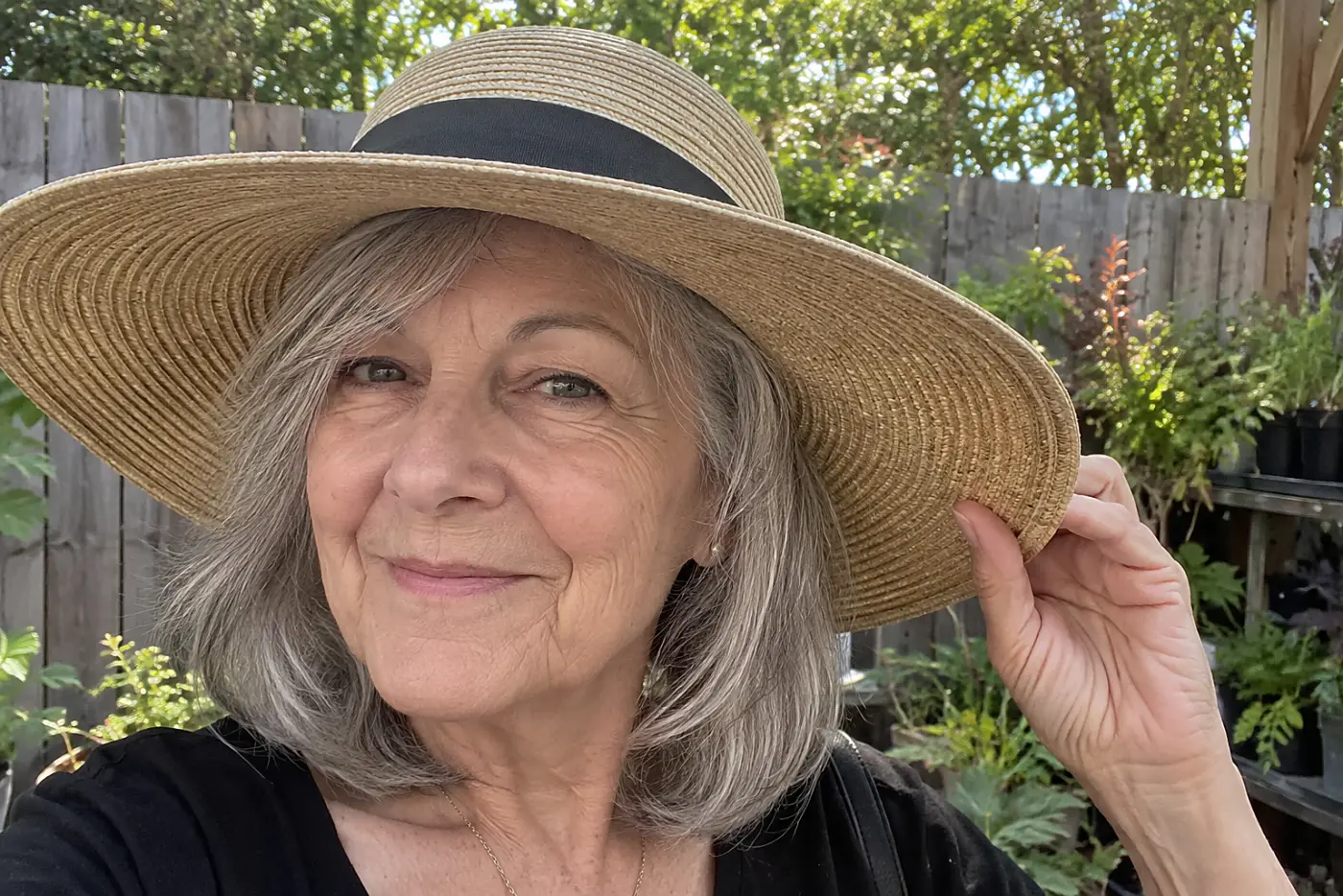 Older woman trying on a wide-brim hat outside a garden shop.
