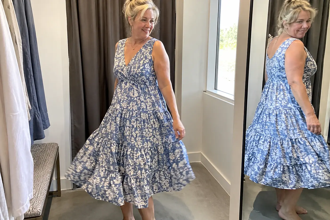 Older woman turning in a tiered midi dress inside a clothing store fitting room.