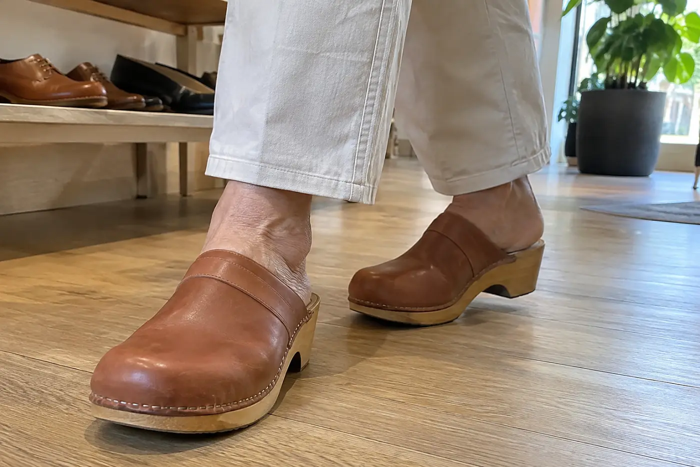 Older woman walking across a shoe-store floor in flat clogs.