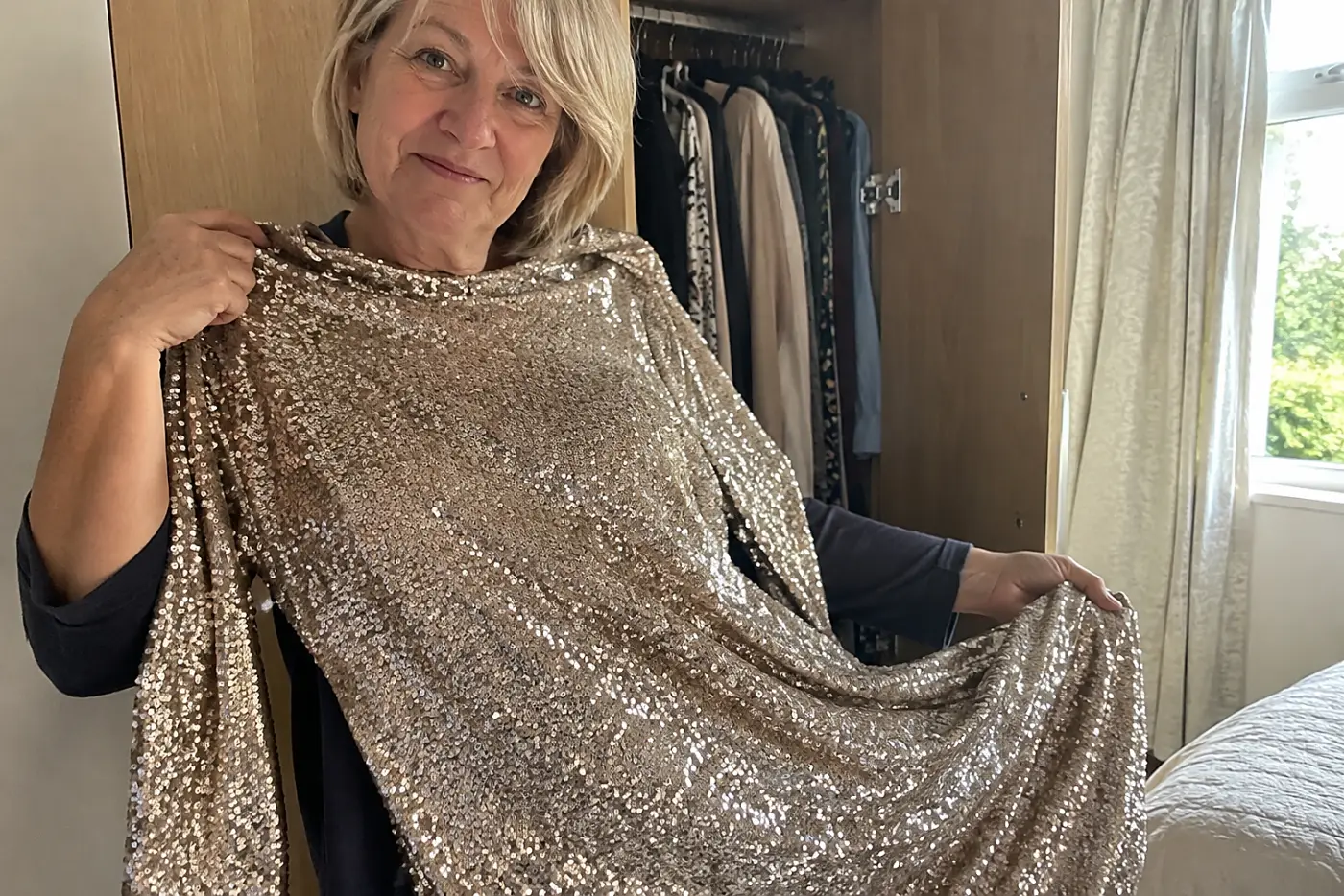 Older woman holding a sequin dress beside her open wardrobe.