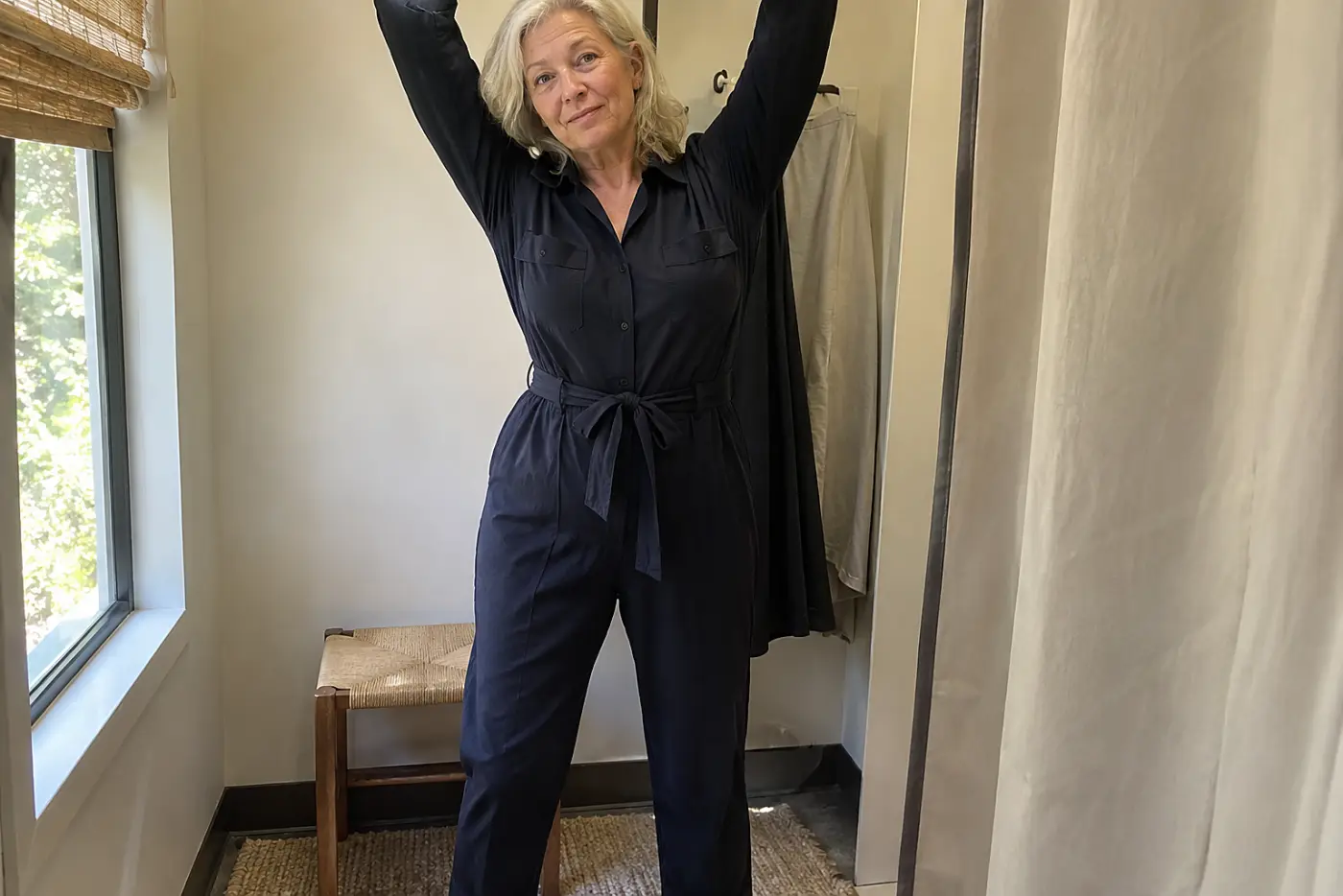 Older woman reaching overhead in a jumpsuit in a fitting room.