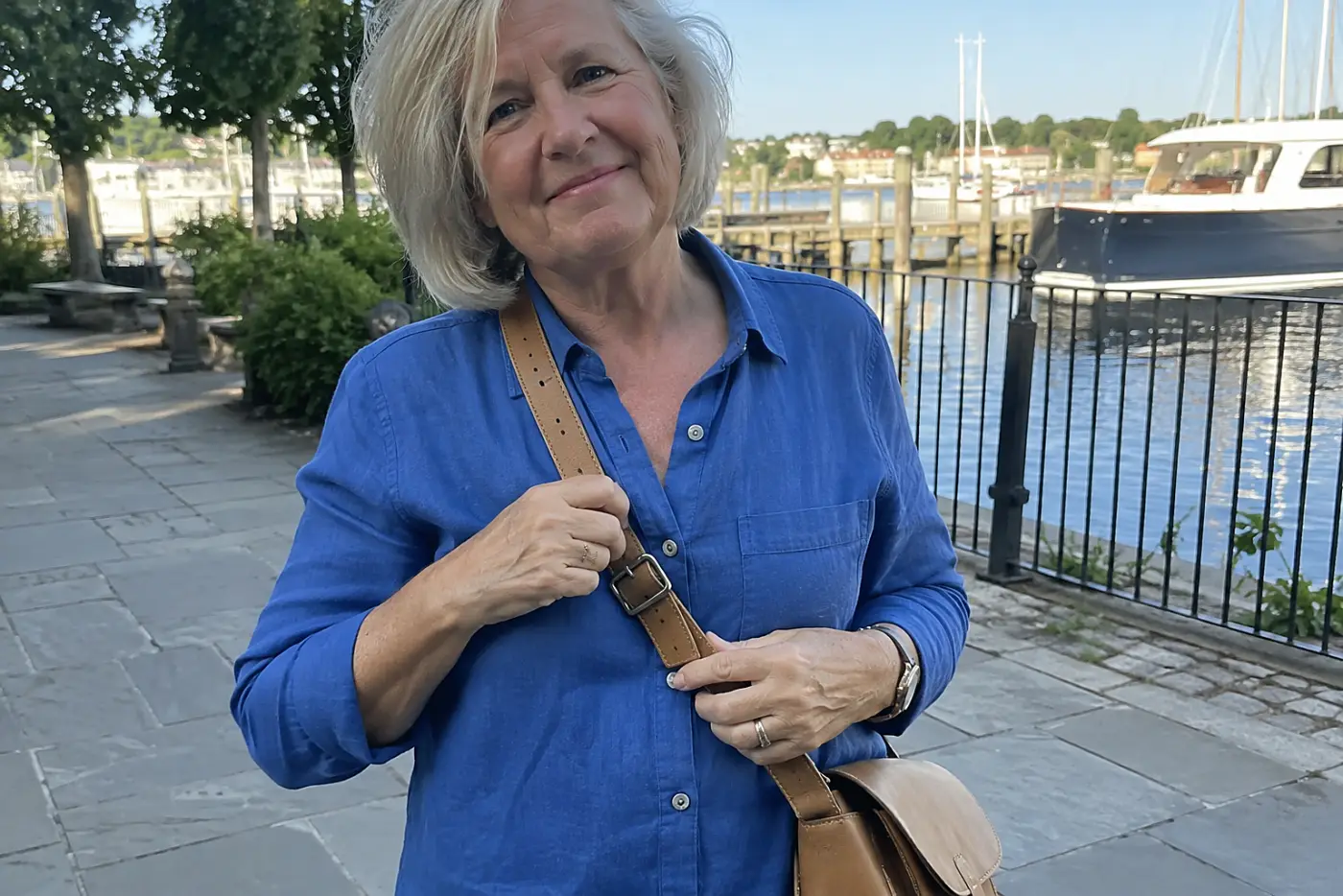 Older woman adjusting a crossbody bag strap on a port town sidewalk.