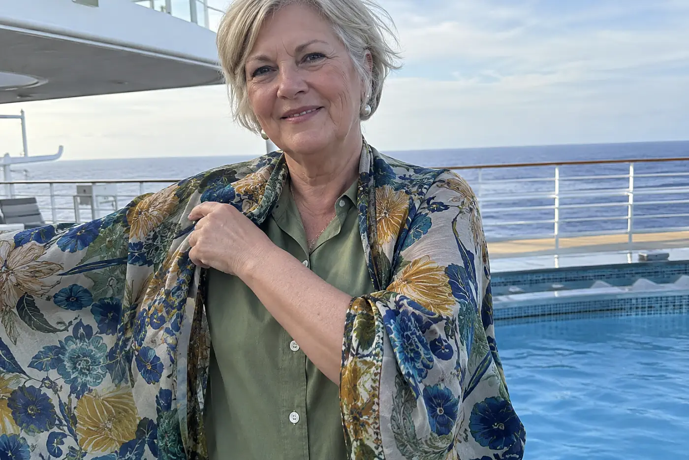 Older woman putting on a kimono-style cover-up beside a ship pool.
