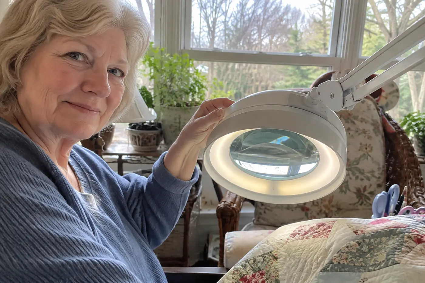 Woman in her sixties positioning a magnifier lamp beside a sewing chair.