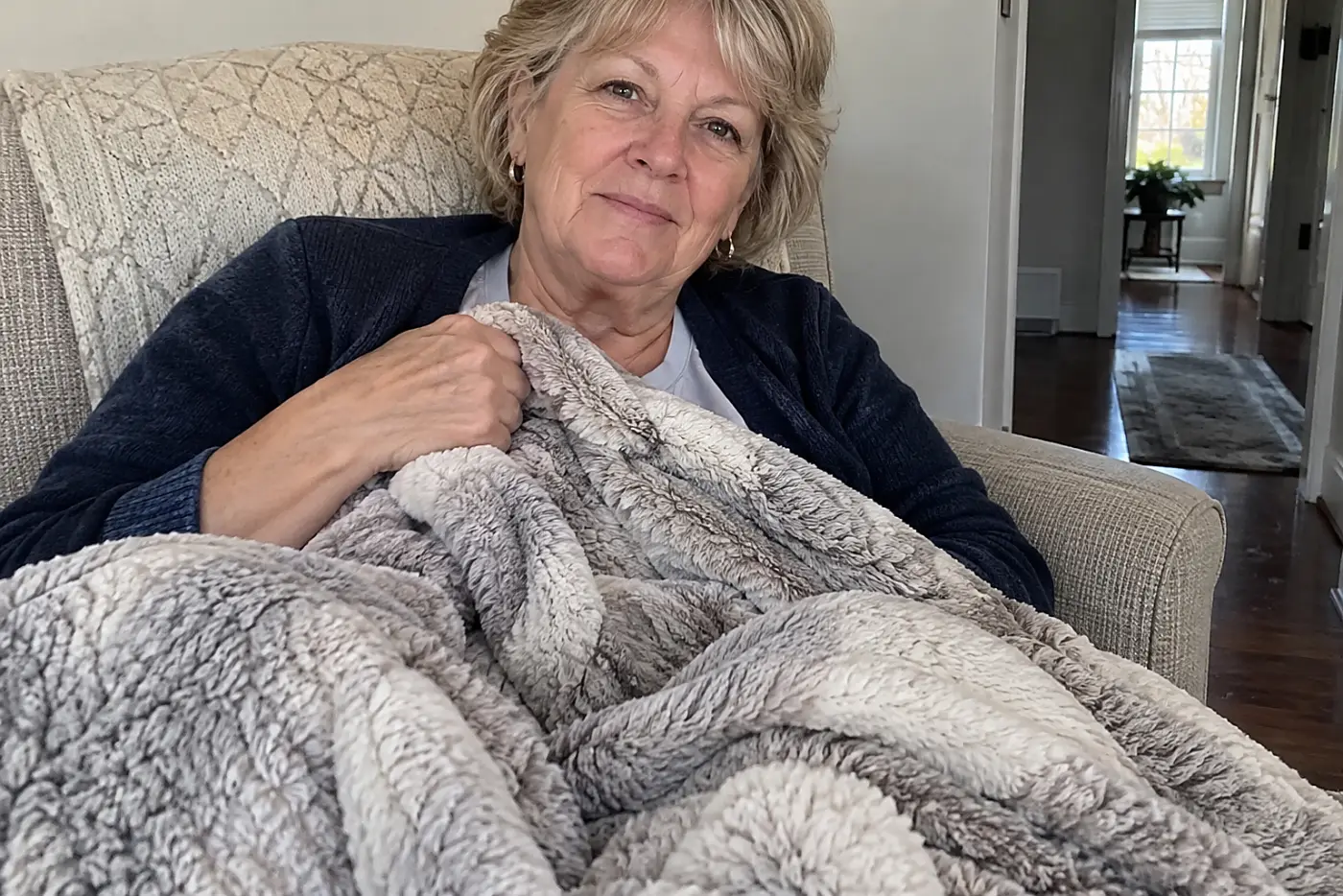 Woman in her sixties pulling a heated throw over her legs in a living room armchair.