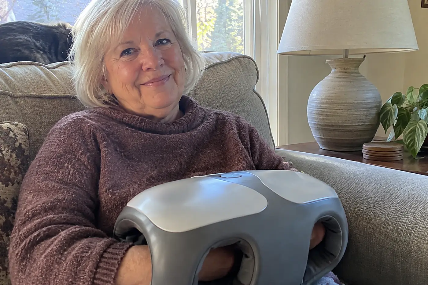 Woman in her sixties warming her hands in a massager beside a living room lamp.