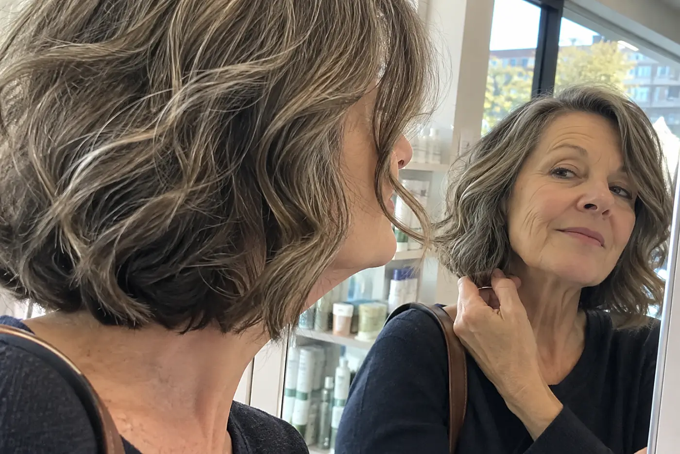 Wavy-haired woman checking the edge of her bob in a pharmacy mirror.