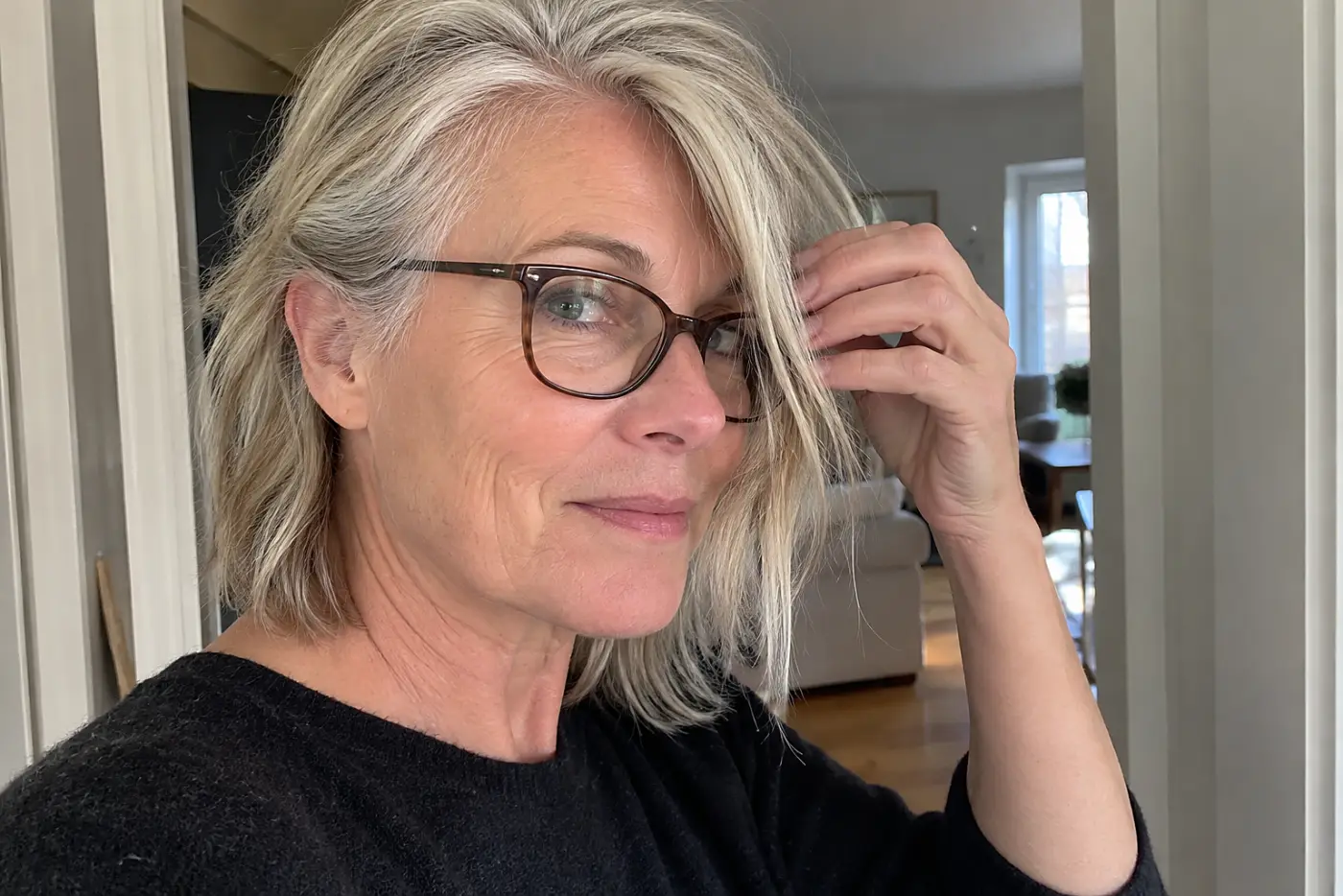 Older woman moving a long front piece away from her glasses in an apartment doorway.