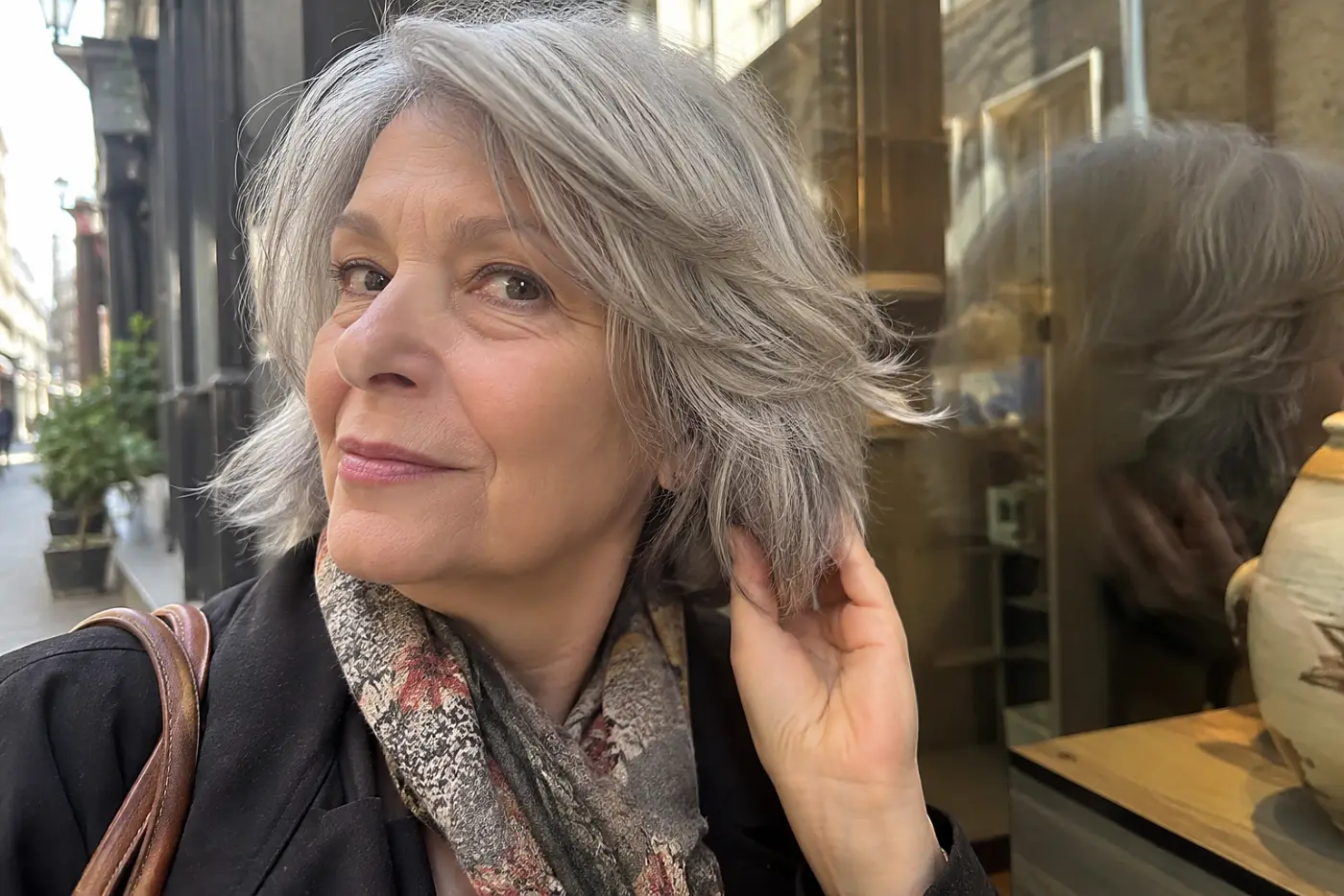 Older woman checking the feathered ends of her hair in a bookstore window.