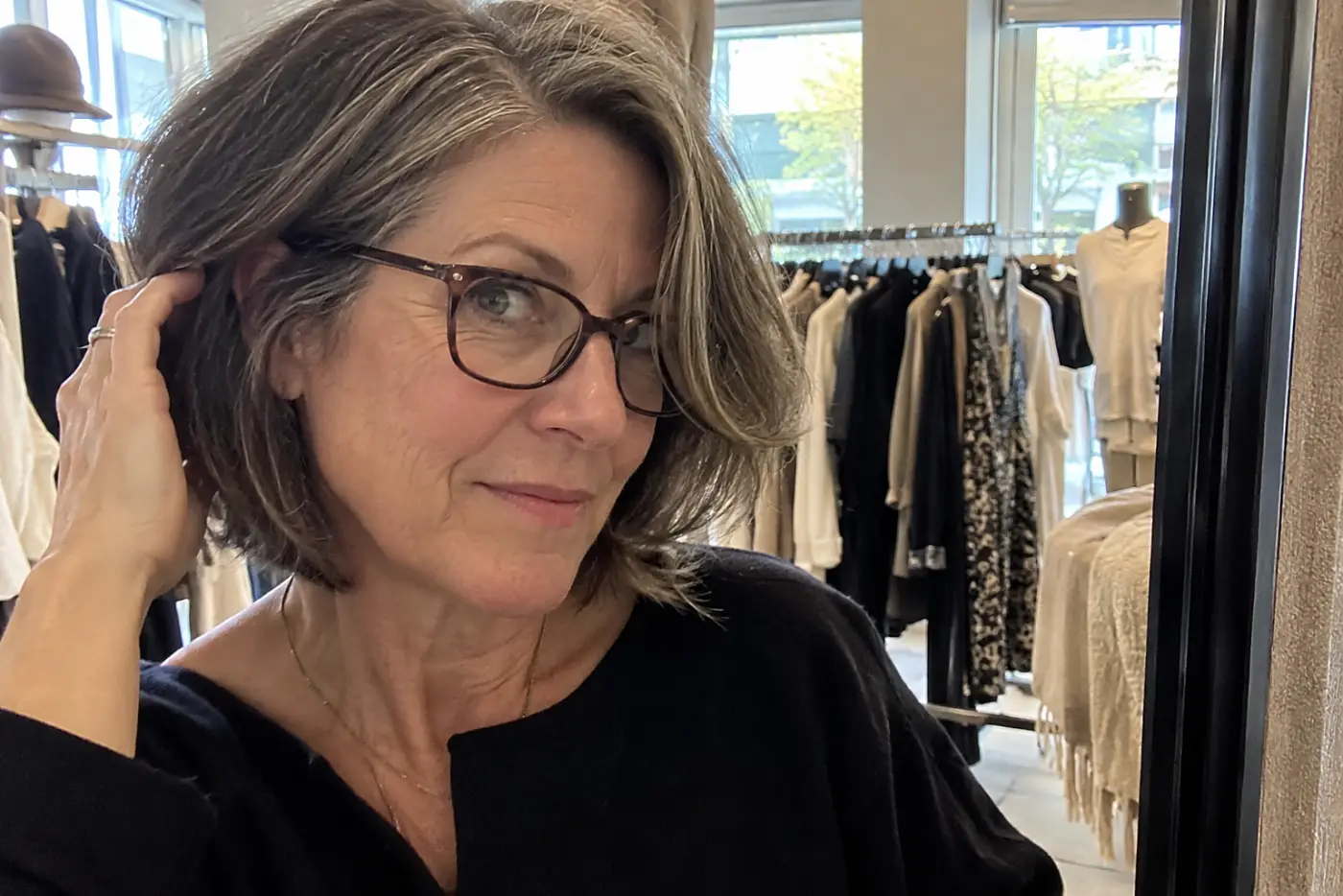Older woman moving her side part while looking into a clothing-store mirror.