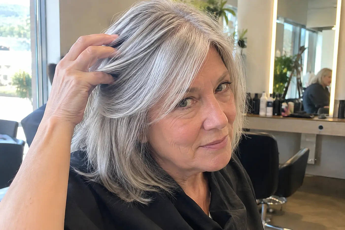 Older woman showing a stylist the part in her hair at a salon station.