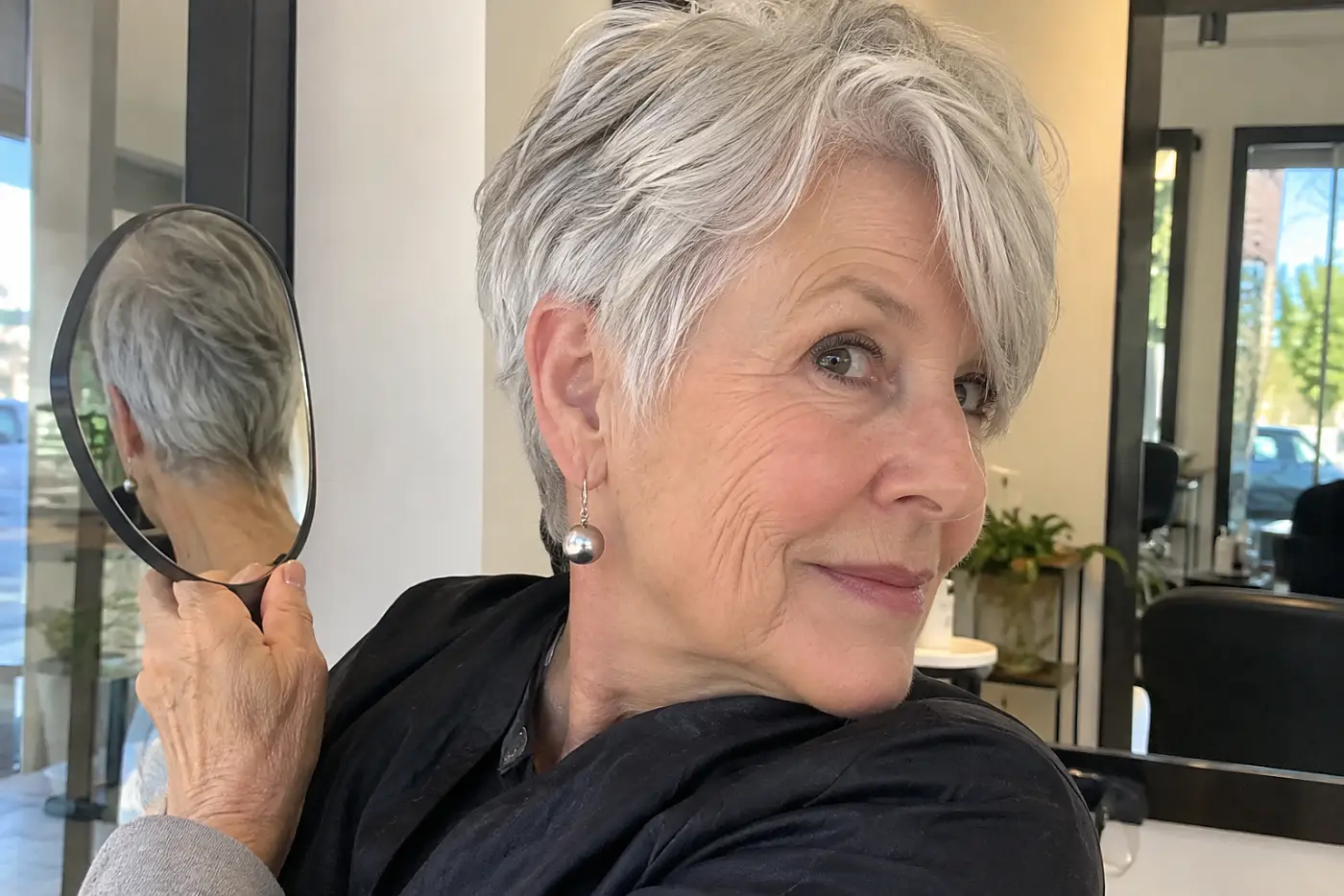 Older woman checking the longer nape of her pixie in a salon hand mirror.