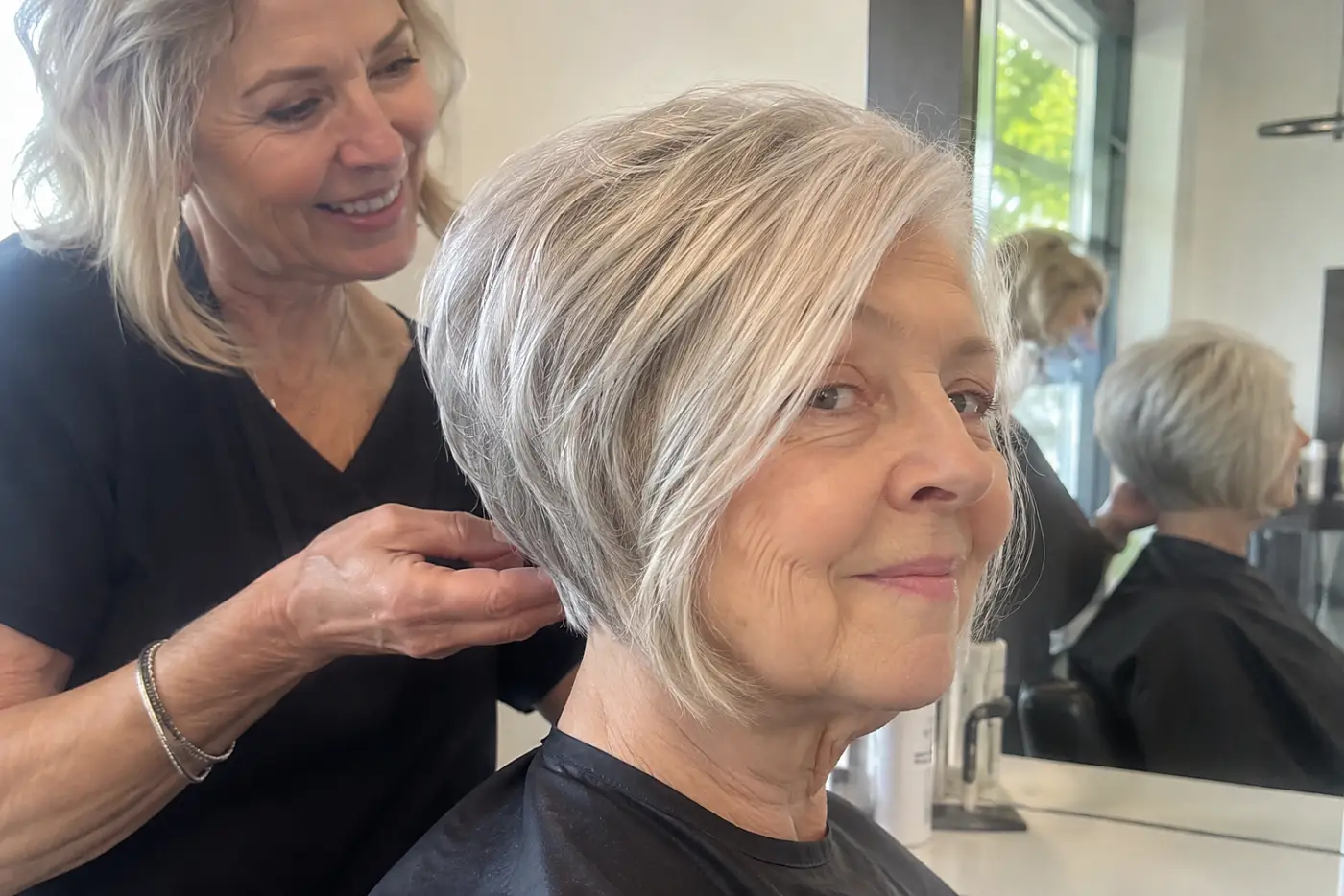 Stylist showing an older woman the nape of her stacked bob at a salon station.