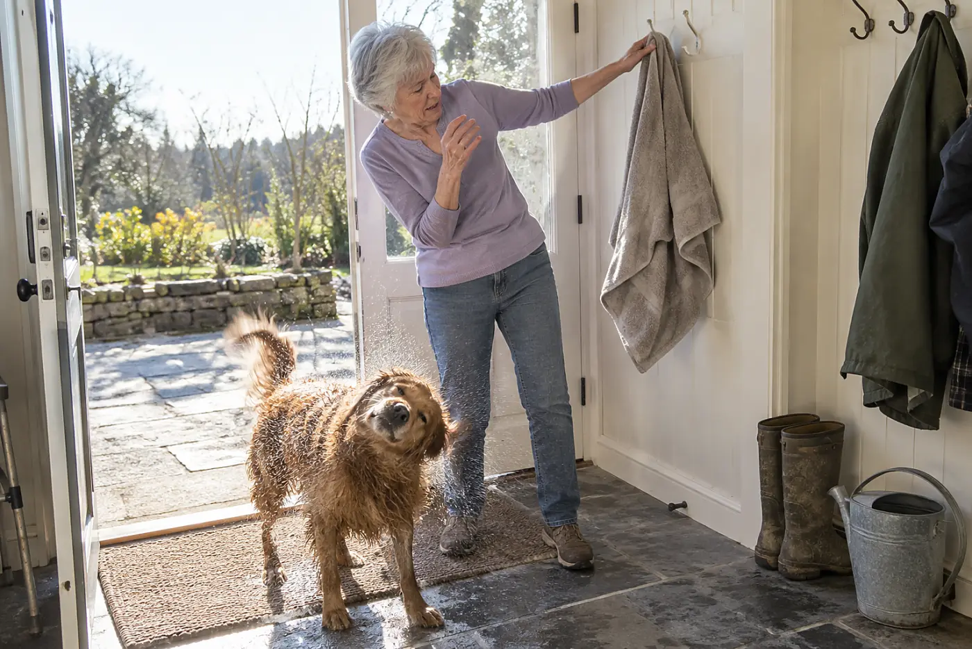 An older woman hangs a damp dog towel on a hook by her back door.