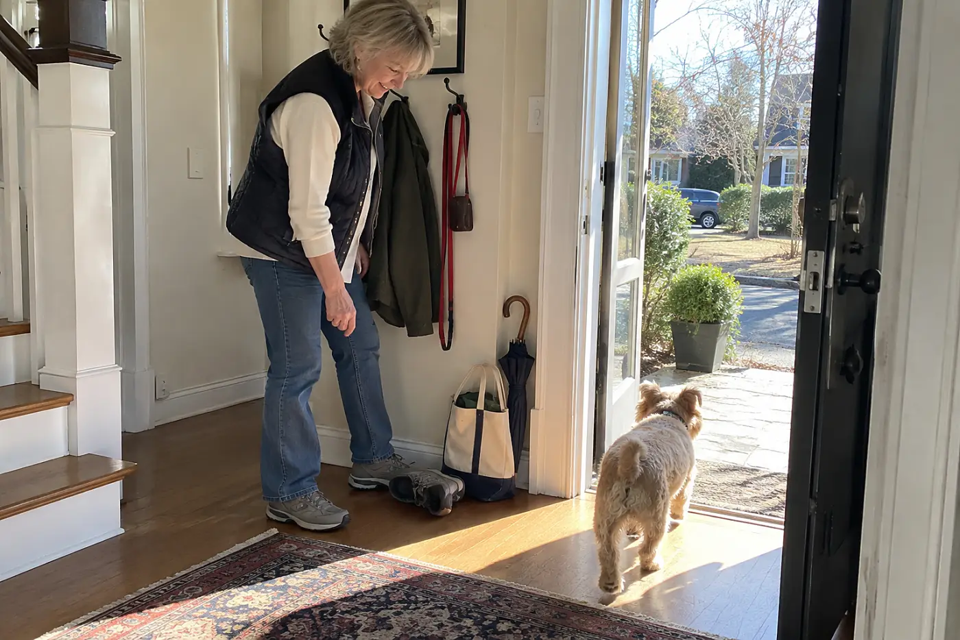 An older woman sets walking shoes beneath a dog leash in her front hall.