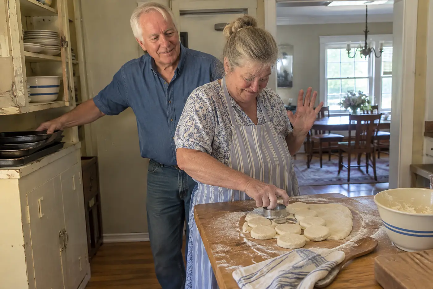 Older woman cuts biscuit dough on a flour-dusted pantry counter.