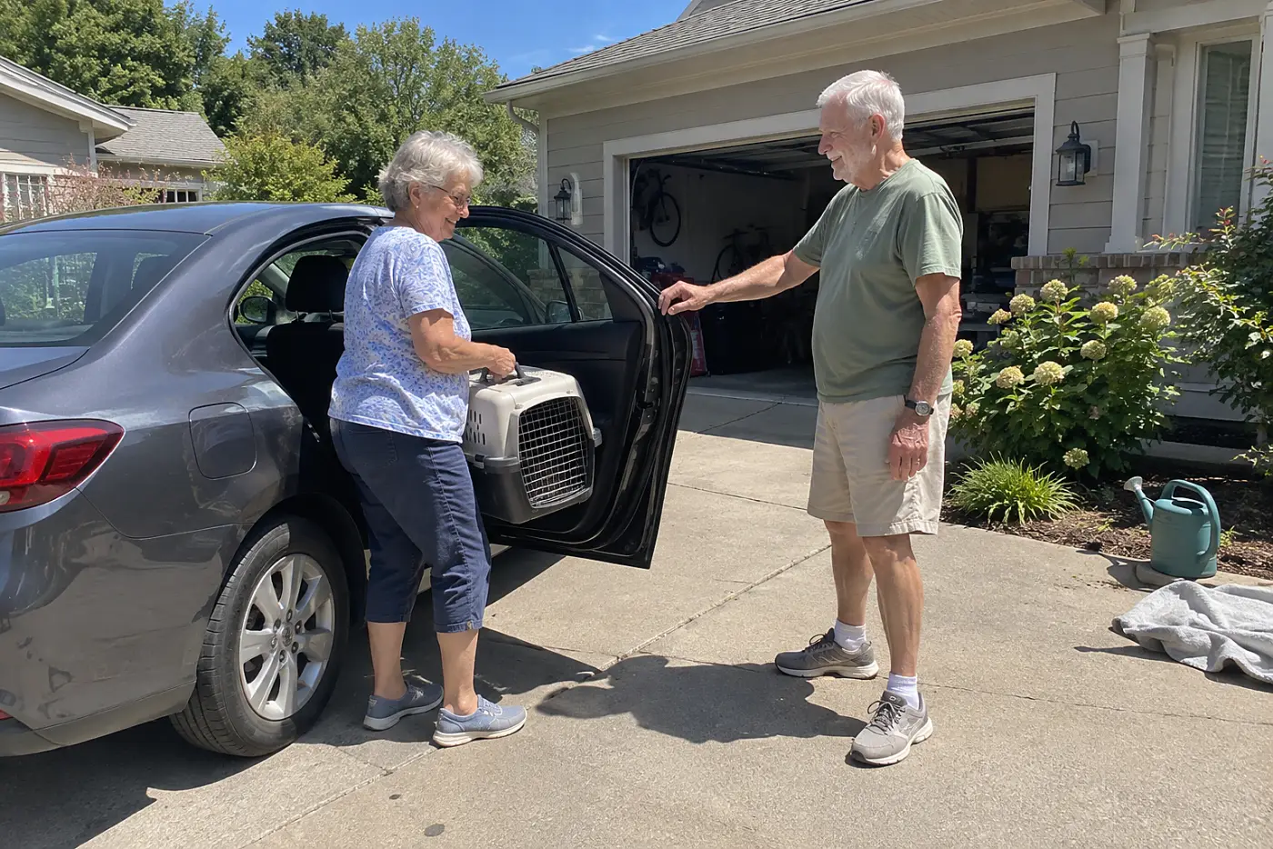 An older woman lifts a pet carrier into the back seat of her parked car.