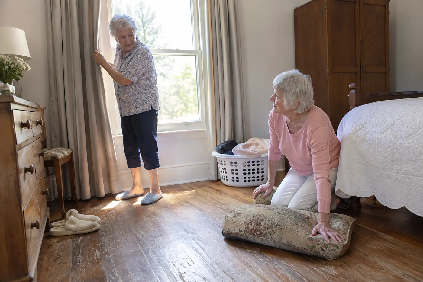 An older woman rests her palm on a worn cushion on her bedroom floor.