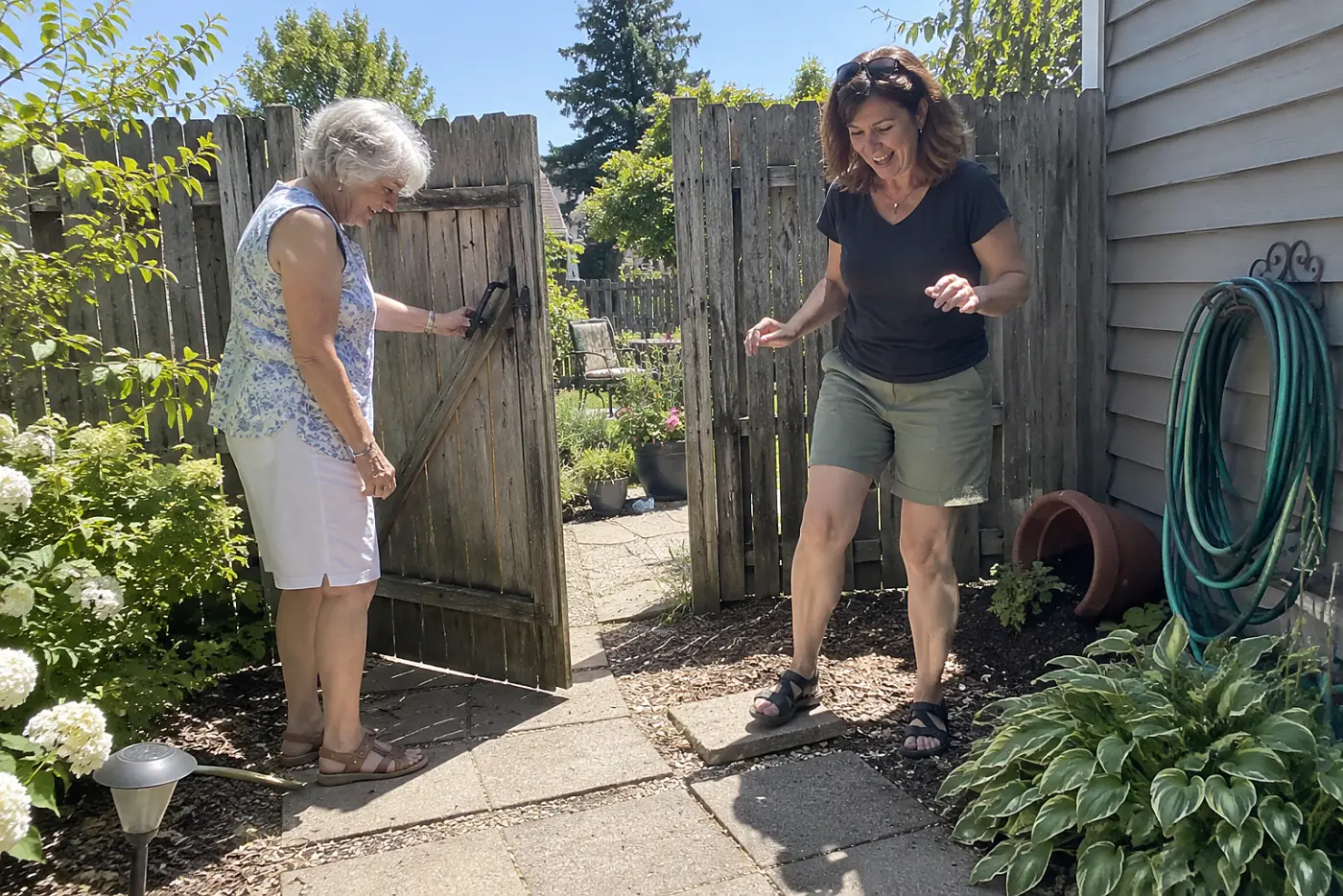 An older woman and her adult daughter stand by the gate to their backyard.