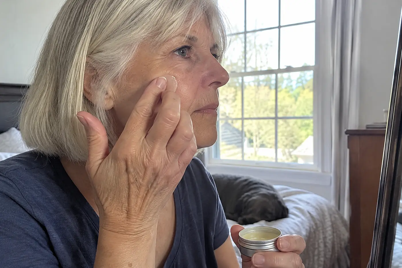 Older woman applying balm to a dry patch in her bedroom.