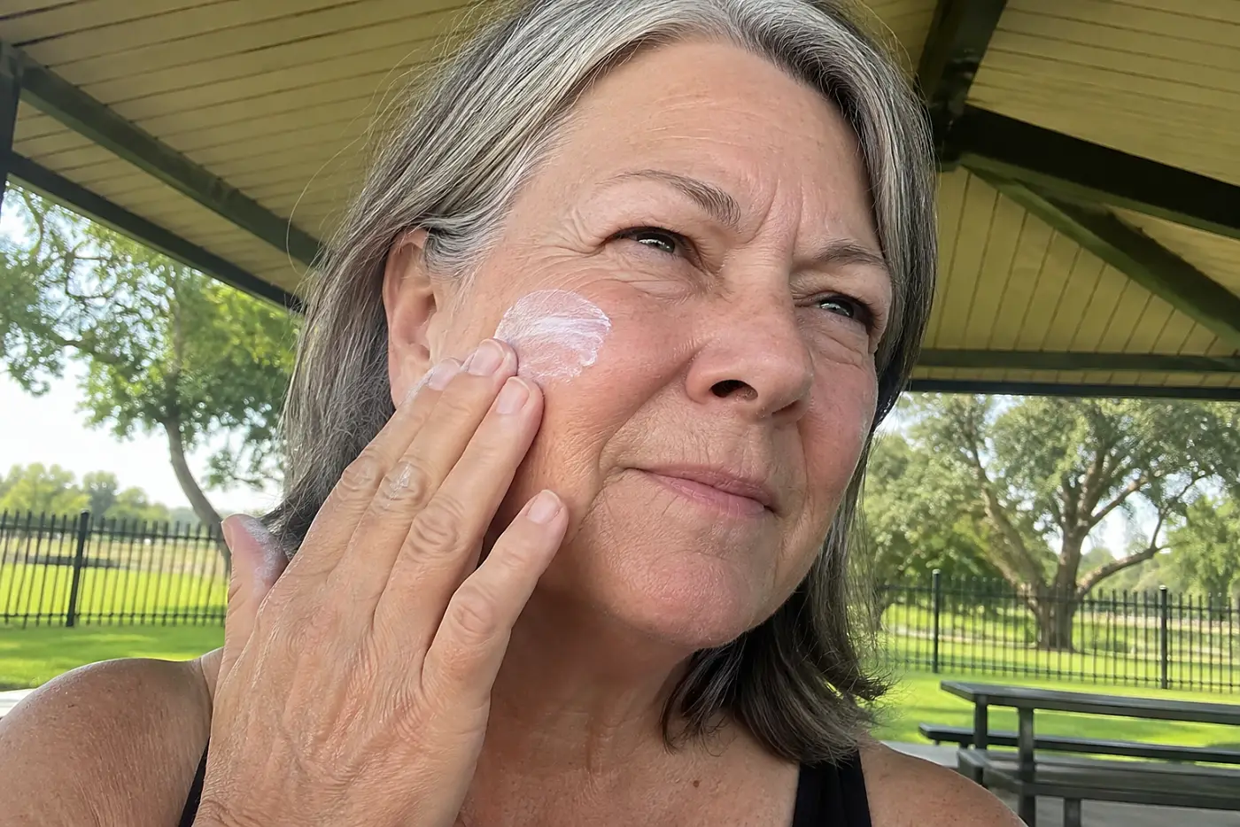 Older woman applying sunscreen beneath a park shelter.