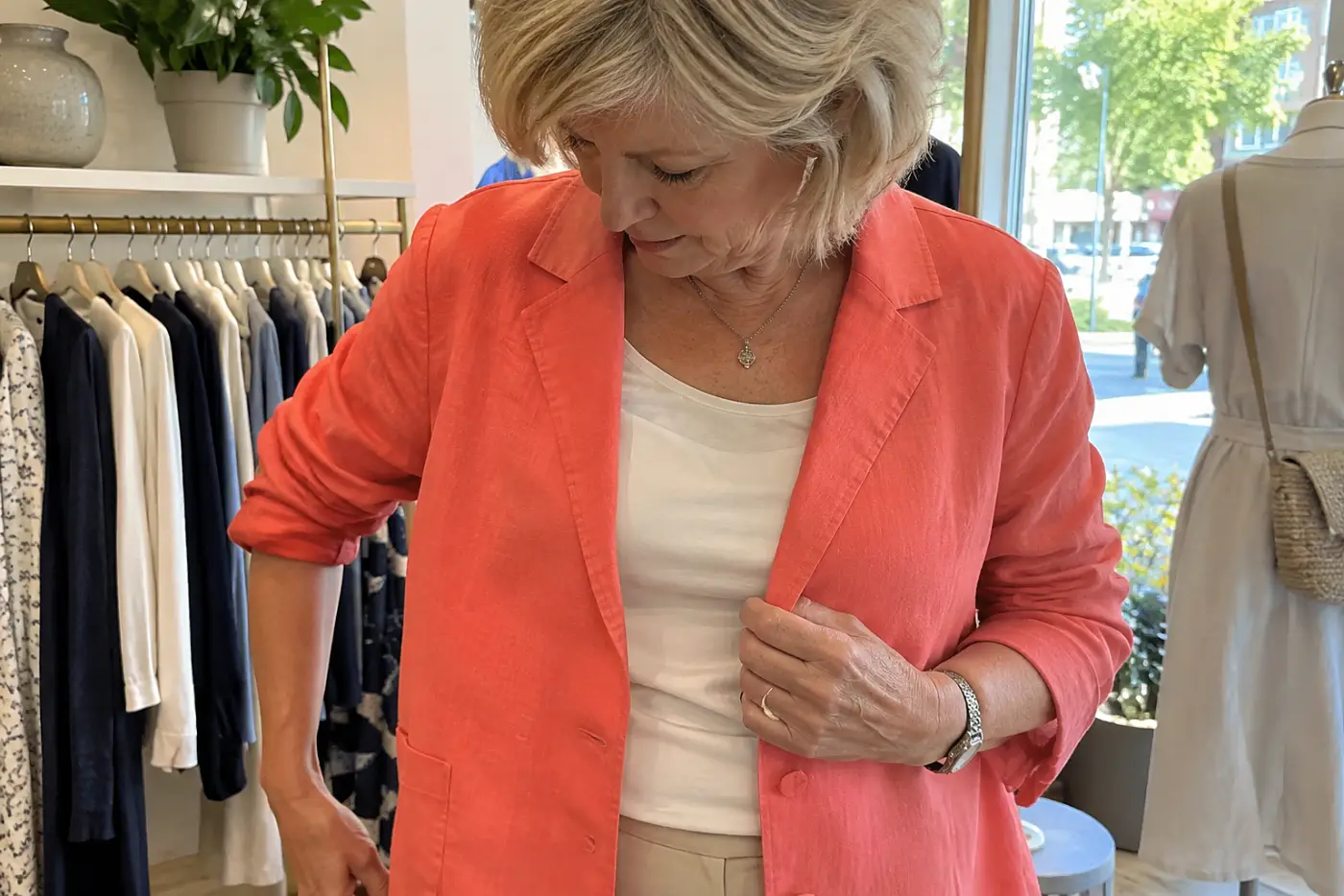 A woman tries a bright jacket over neutral clothes in a clothing shop.