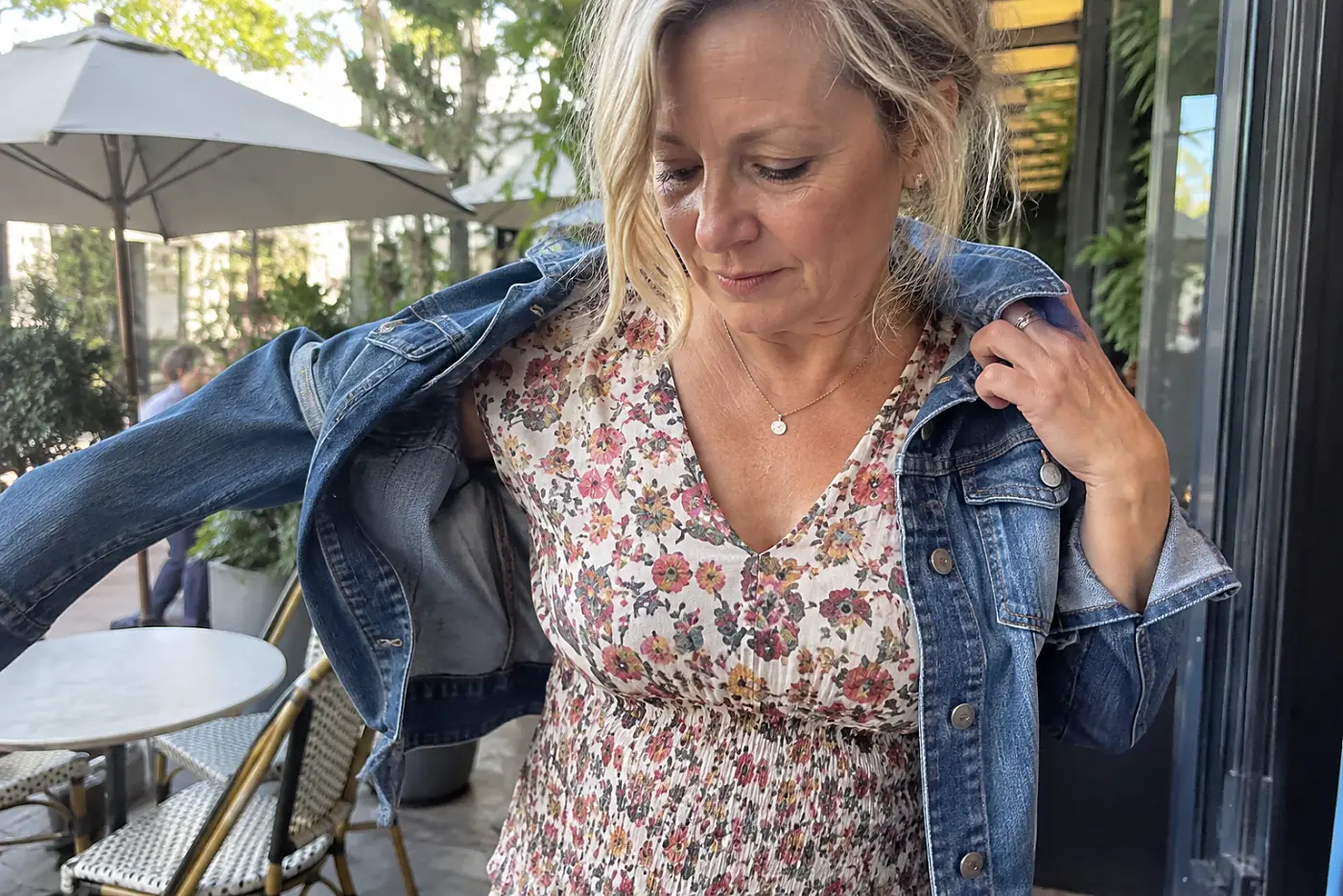 A woman slips on a denim jacket over a midi dress outside a neighborhood café.