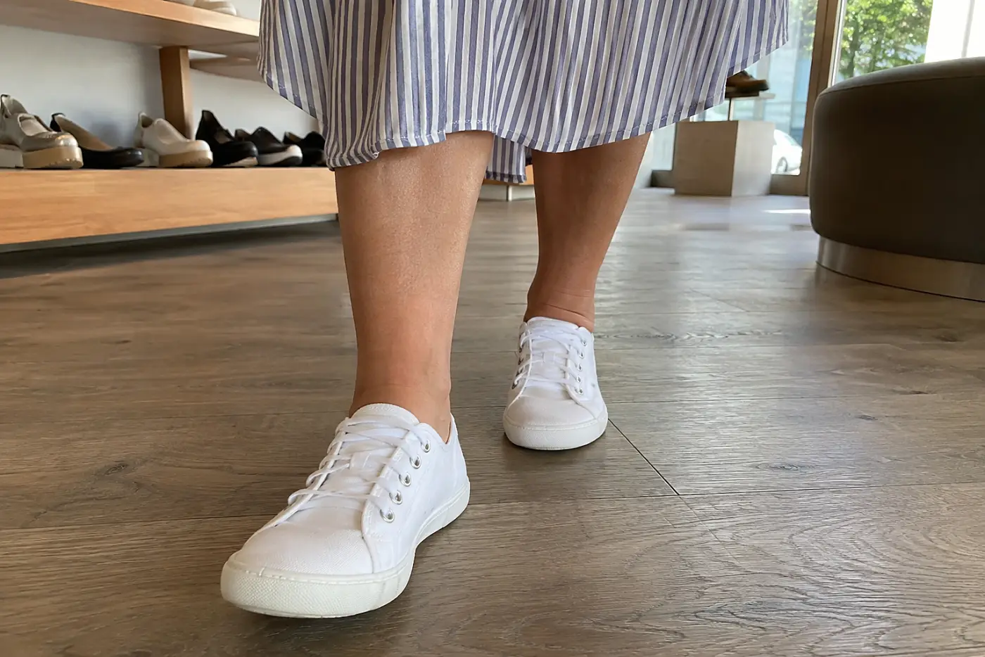 A woman walks around a shoe shop in white canvas sneakers and a shirtdress.