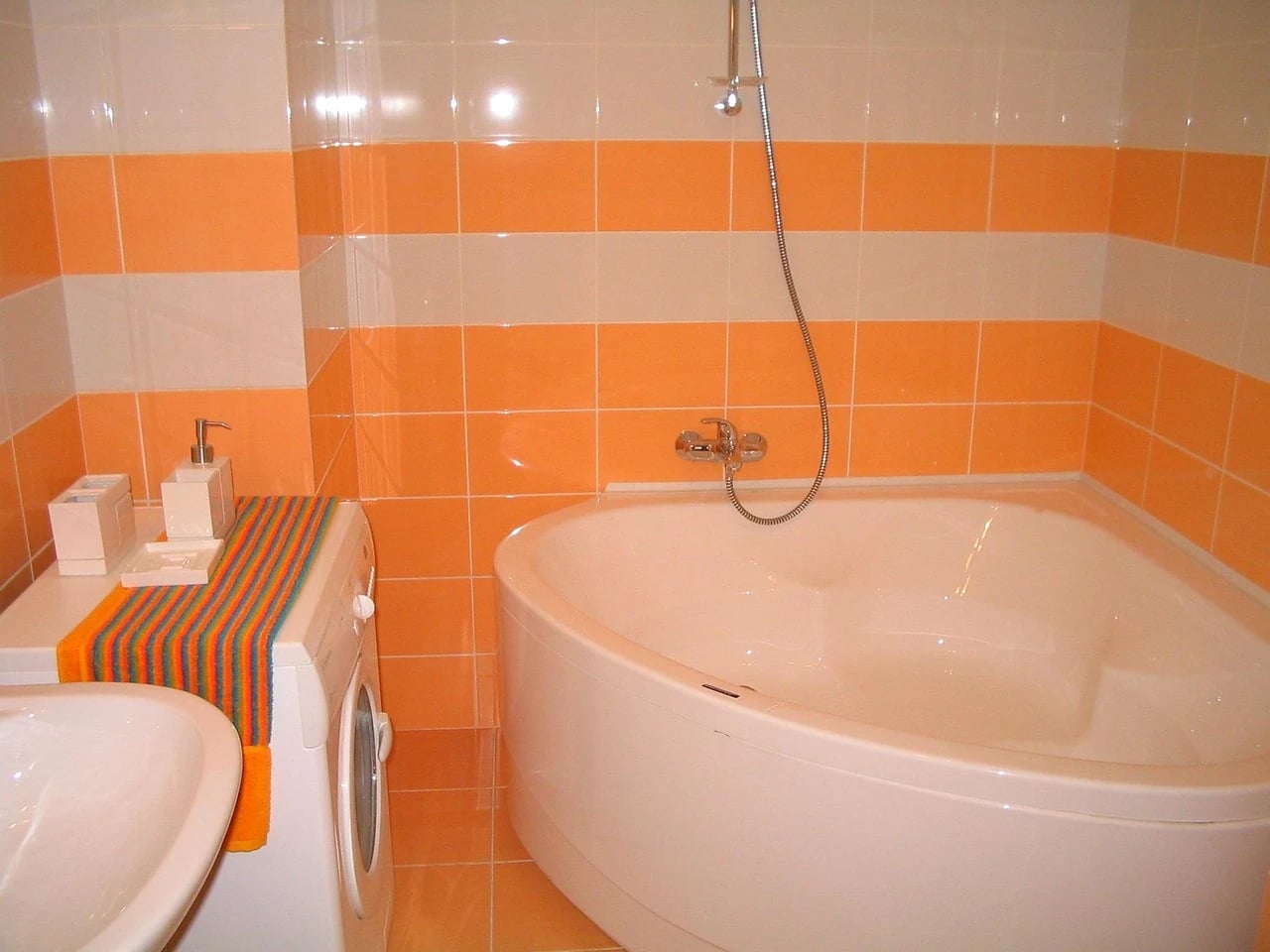 Bathroom with horizontal bands of orange and cream tile, a corner bathtub, washing machine and striped towel