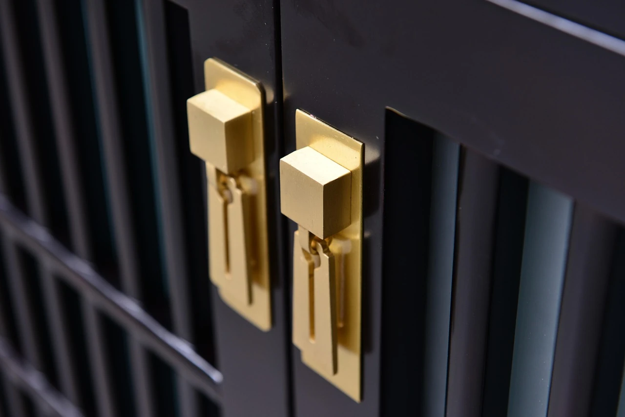 Close-up of brushed gold drop handles on dark wood cabinet doors with slatted panels
