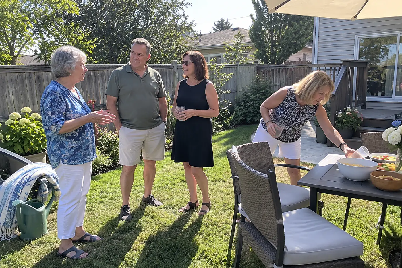 Older woman speaking with guests while her daughter stands nearby at a backyard party.