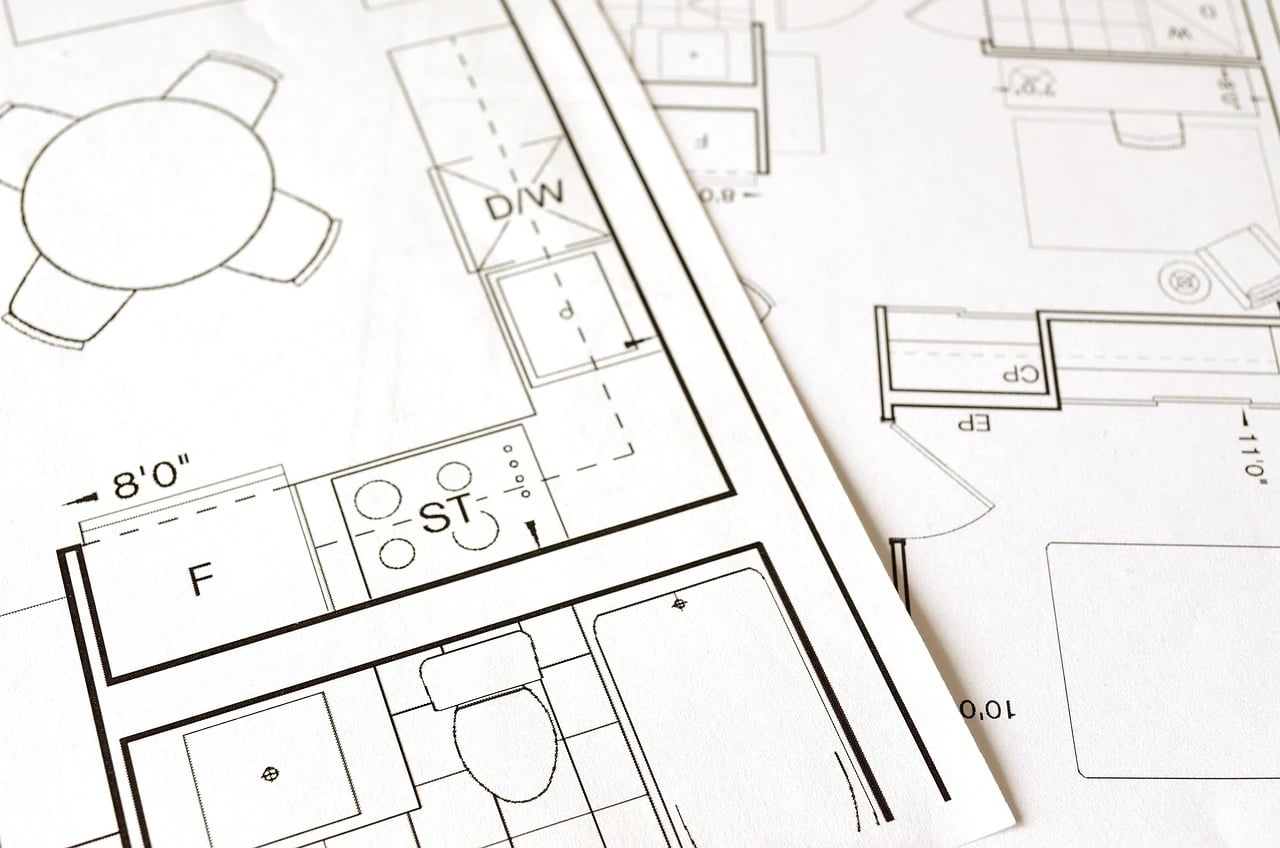 Close-up of printed house floor plans showing a bathroom layout with toilet, tub, sink, and kitchen dimensions