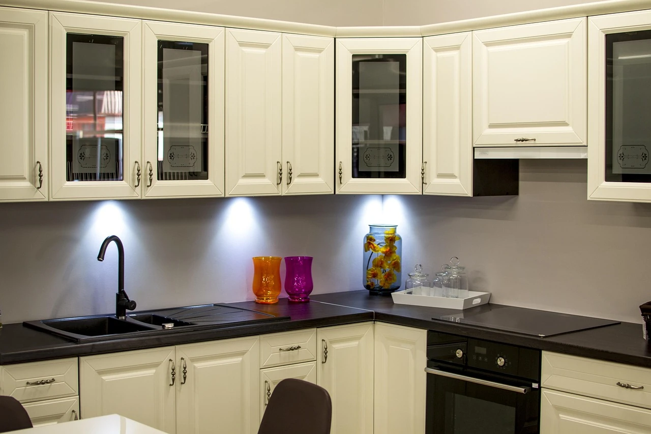 White kitchen cabinets with under-cabinet lights glowing over a dark counter, sink, colorful vases and a flower jar