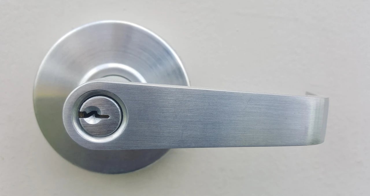 Close-up of a brushed steel lever door handle with a keyhole on a pale wall