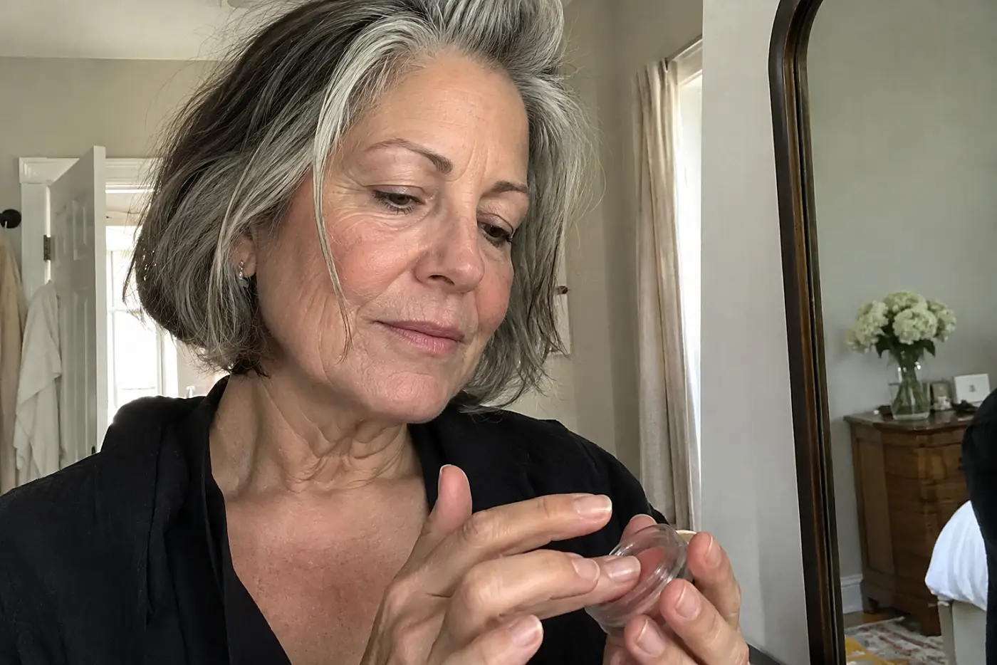 Woman warming balm between her fingers in front of a dressing-room mirror.