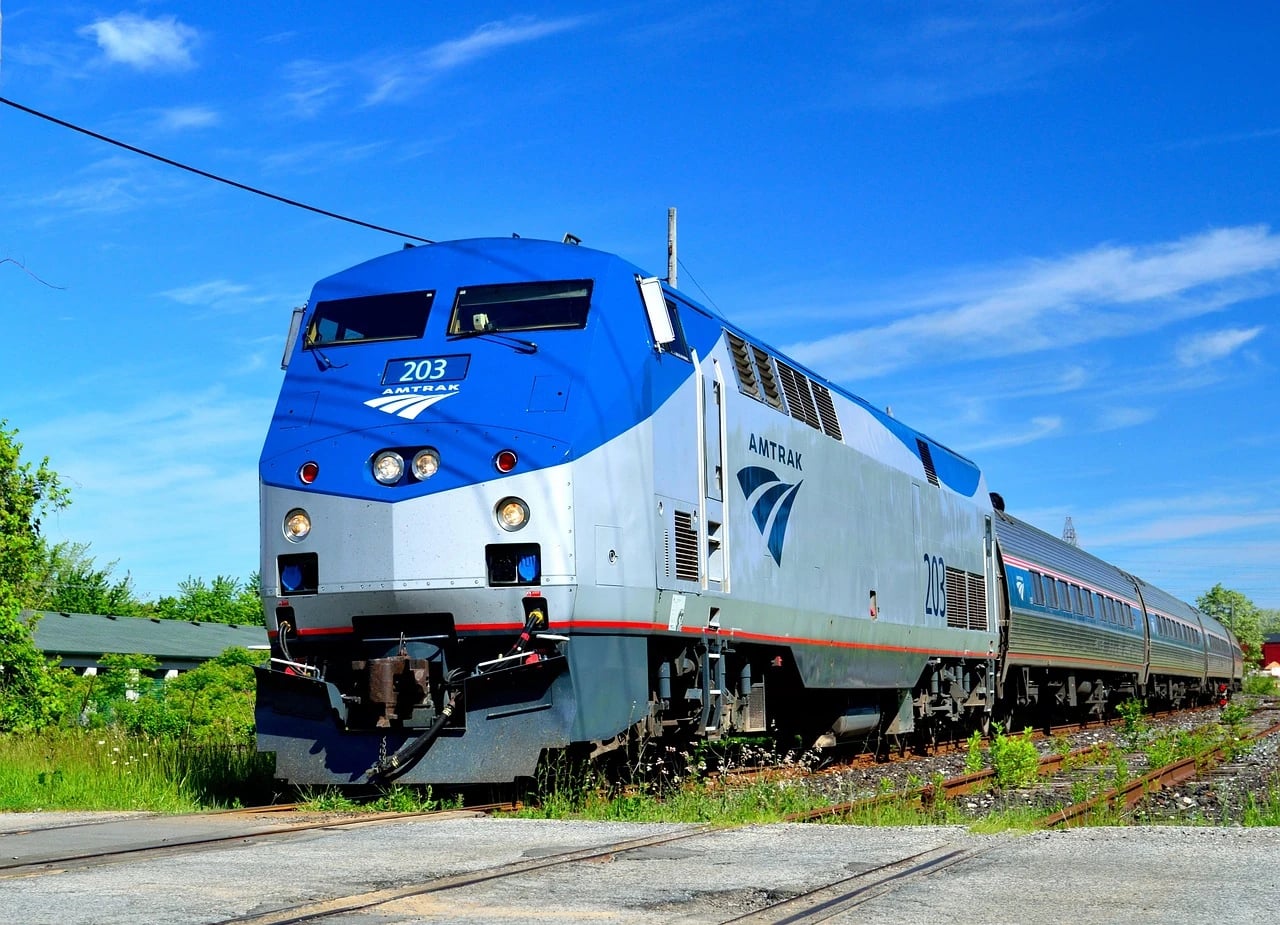 Blue and silver Amtrak locomotive number 203 pulling passenger cars along a track under a bright blue sky