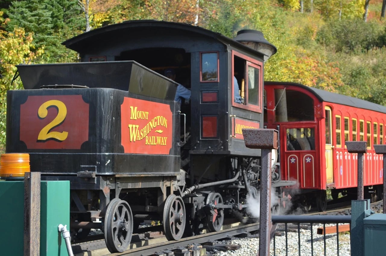 Black steam locomotive number 2 of the Mount Washington Railway pulling a red passenger car past autumn foliage