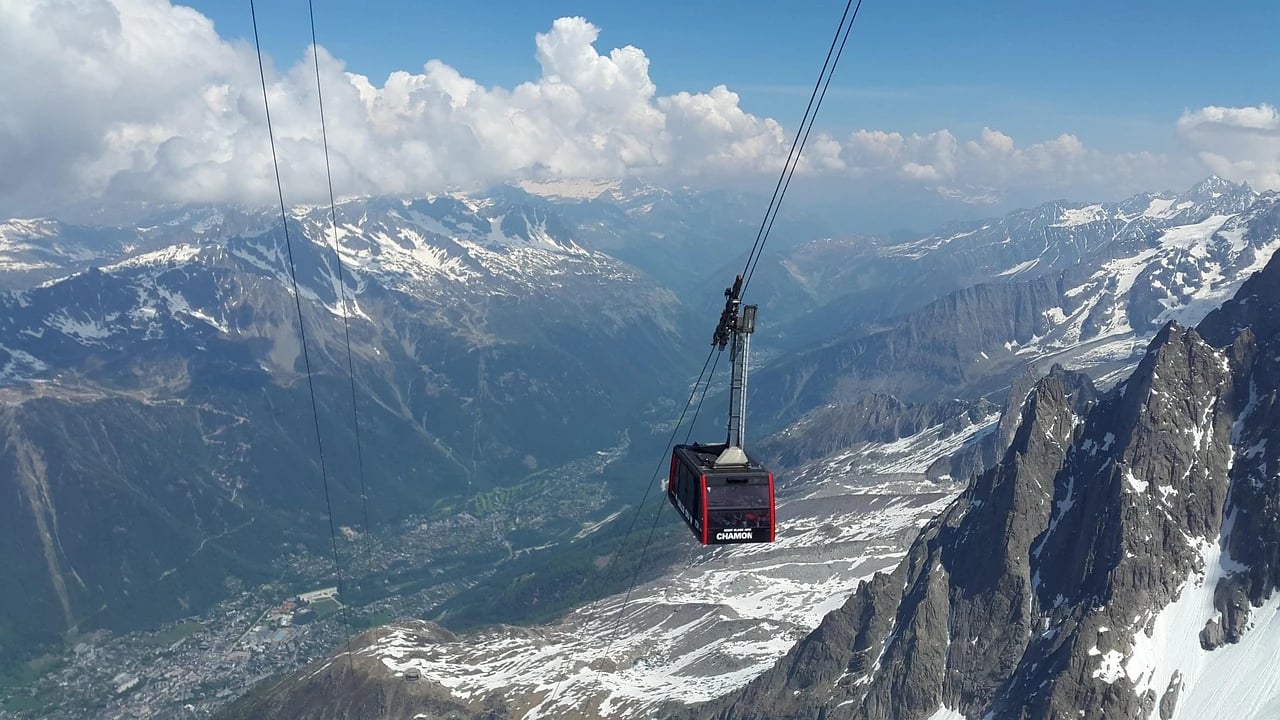 Red cable car cabin above snowy Alpine peaks with the Chamonix valley and town far below